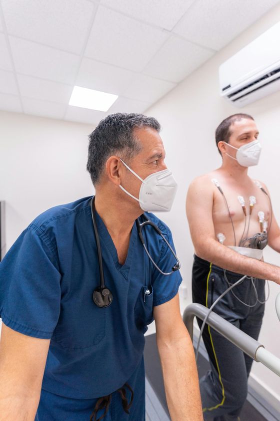 Two masked clinicians in scrubs attending to a patient in a hospital room