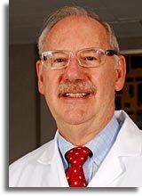 Portrait of a smiling doctor in a white coat, glasses, and red tie.