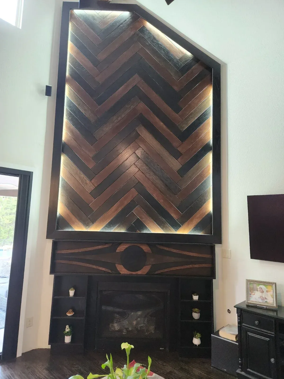 Fireplace with herringbone wood paneling and built-in lighting. Dark wood mantel with side shelves.