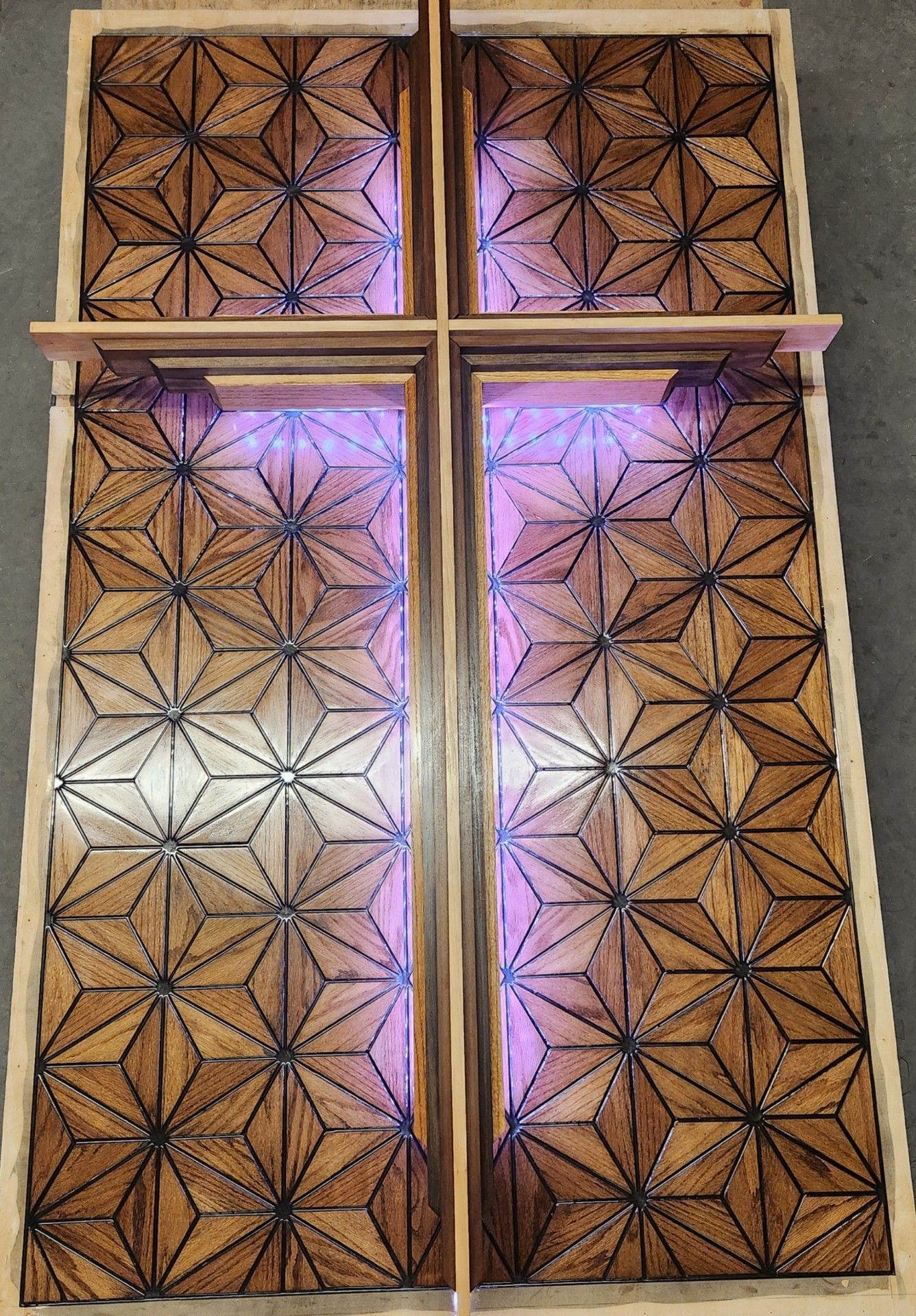 Wooden cross sculpture with star-patterned inlay, lit from behind with purple light.