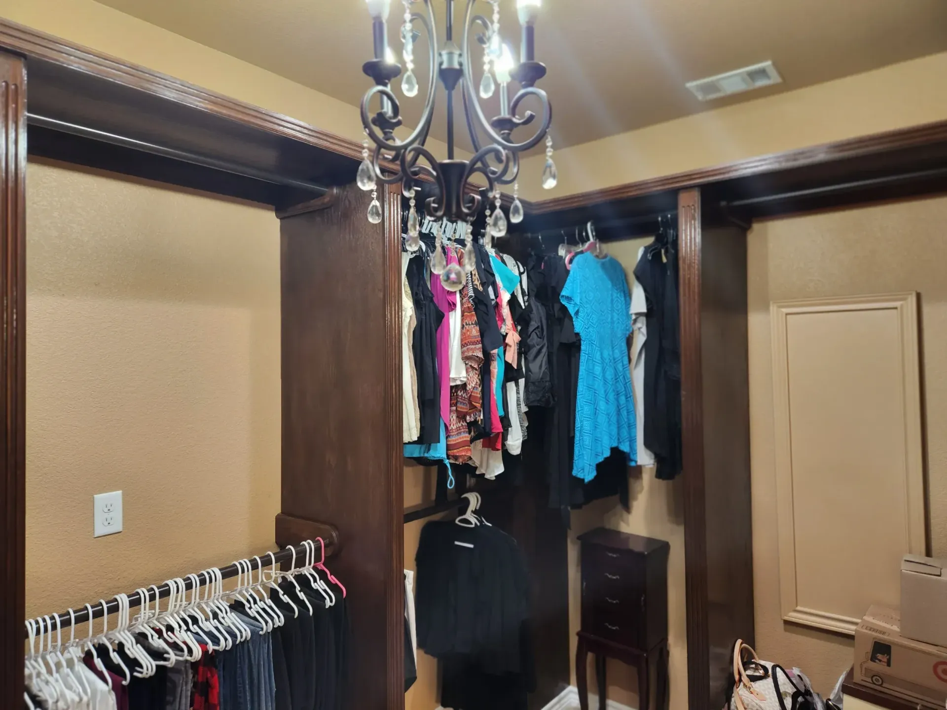 A walk-in closet with hanging clothes, ornate wood trim, a chandelier, and beige walls.