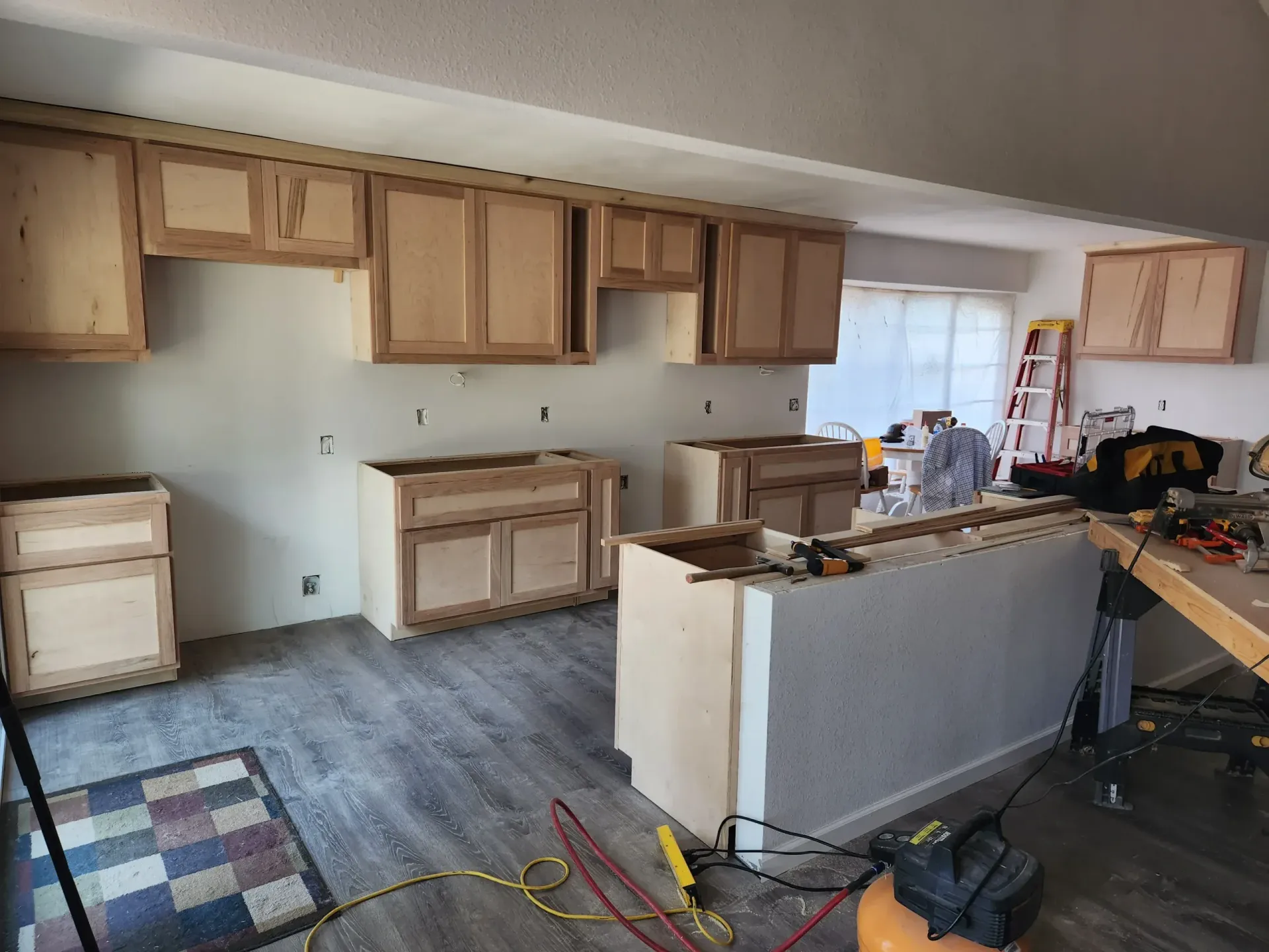 Kitchen renovation in progress: bare wood cabinets installed, gray walls, light gray floor, tools present.