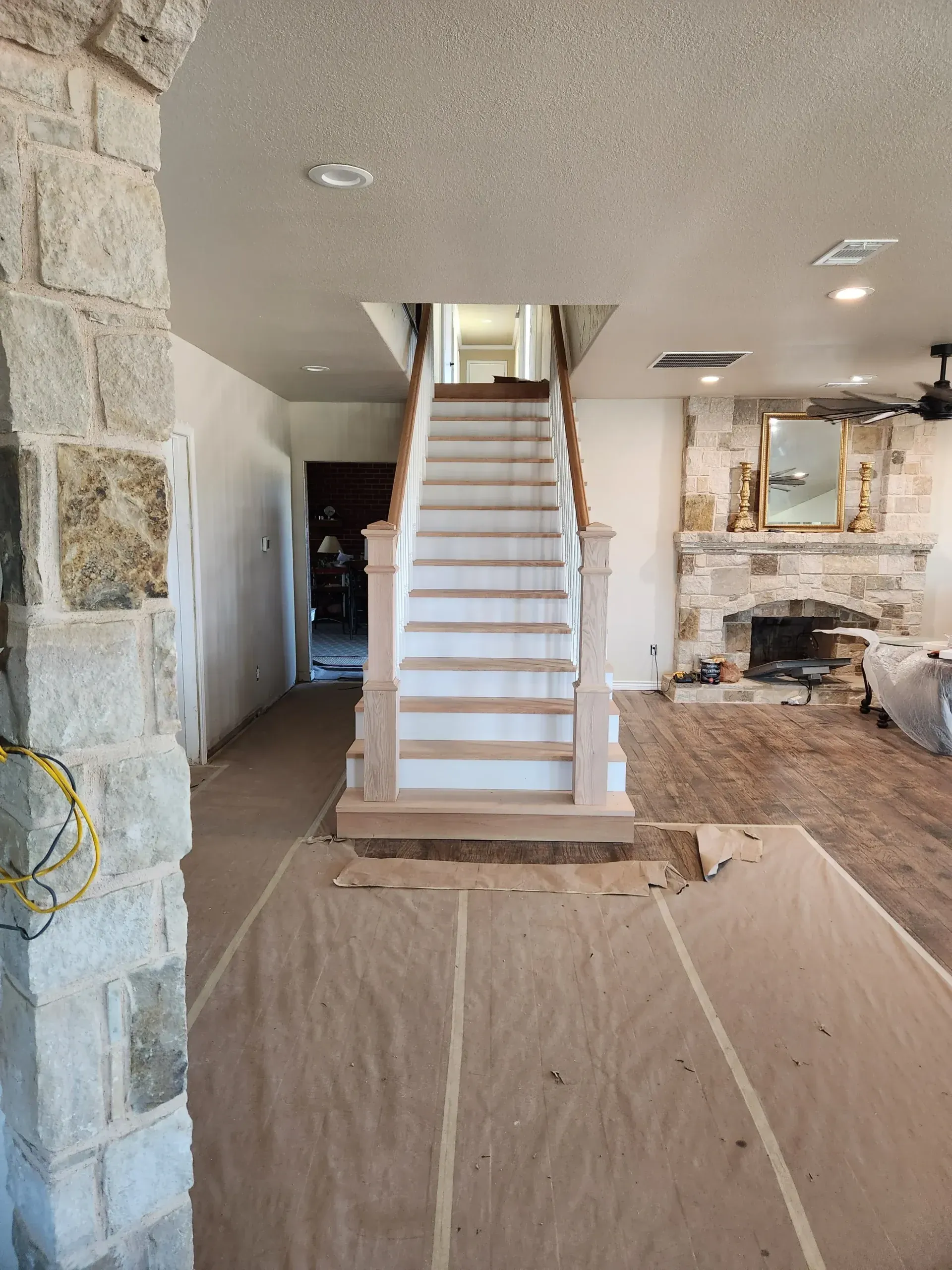 Interior view of a home renovation in progress with stairs, stone accents, and protective floor covering.