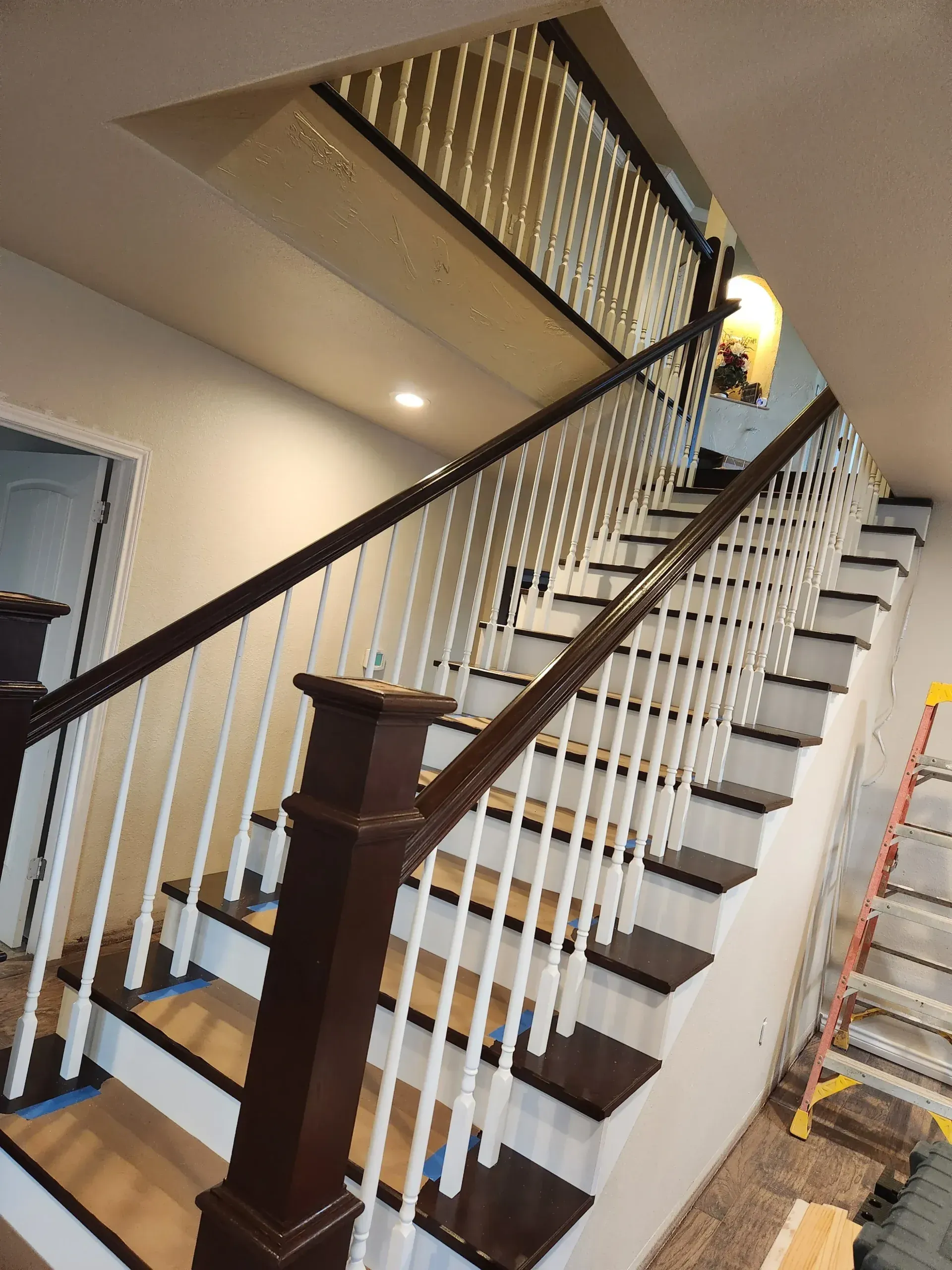 Newly painted staircase with dark brown handrails and white spindles, leading upwards.