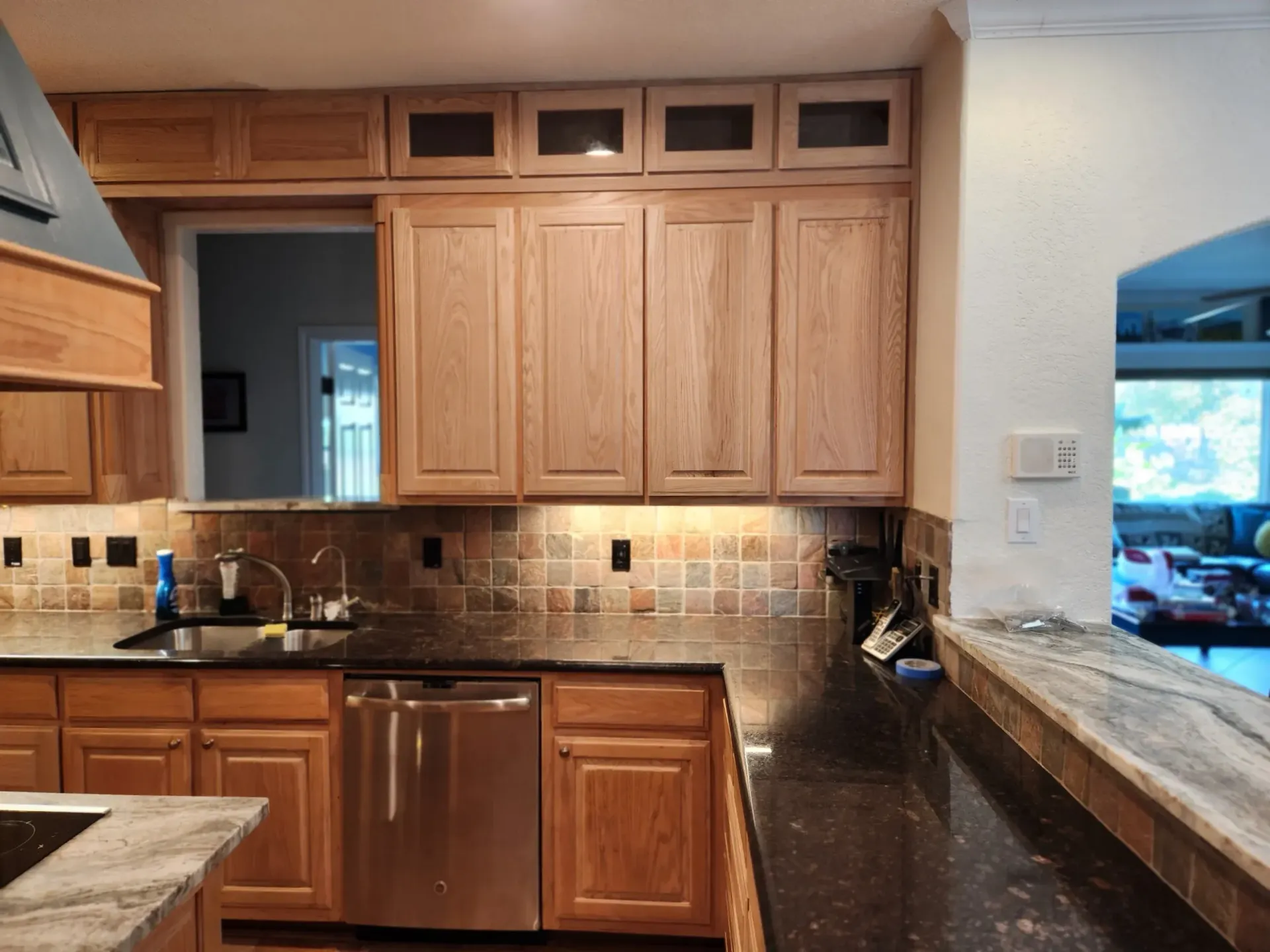 Wooden kitchen cabinets above a dark countertop and sink. Stainless steel dishwasher.