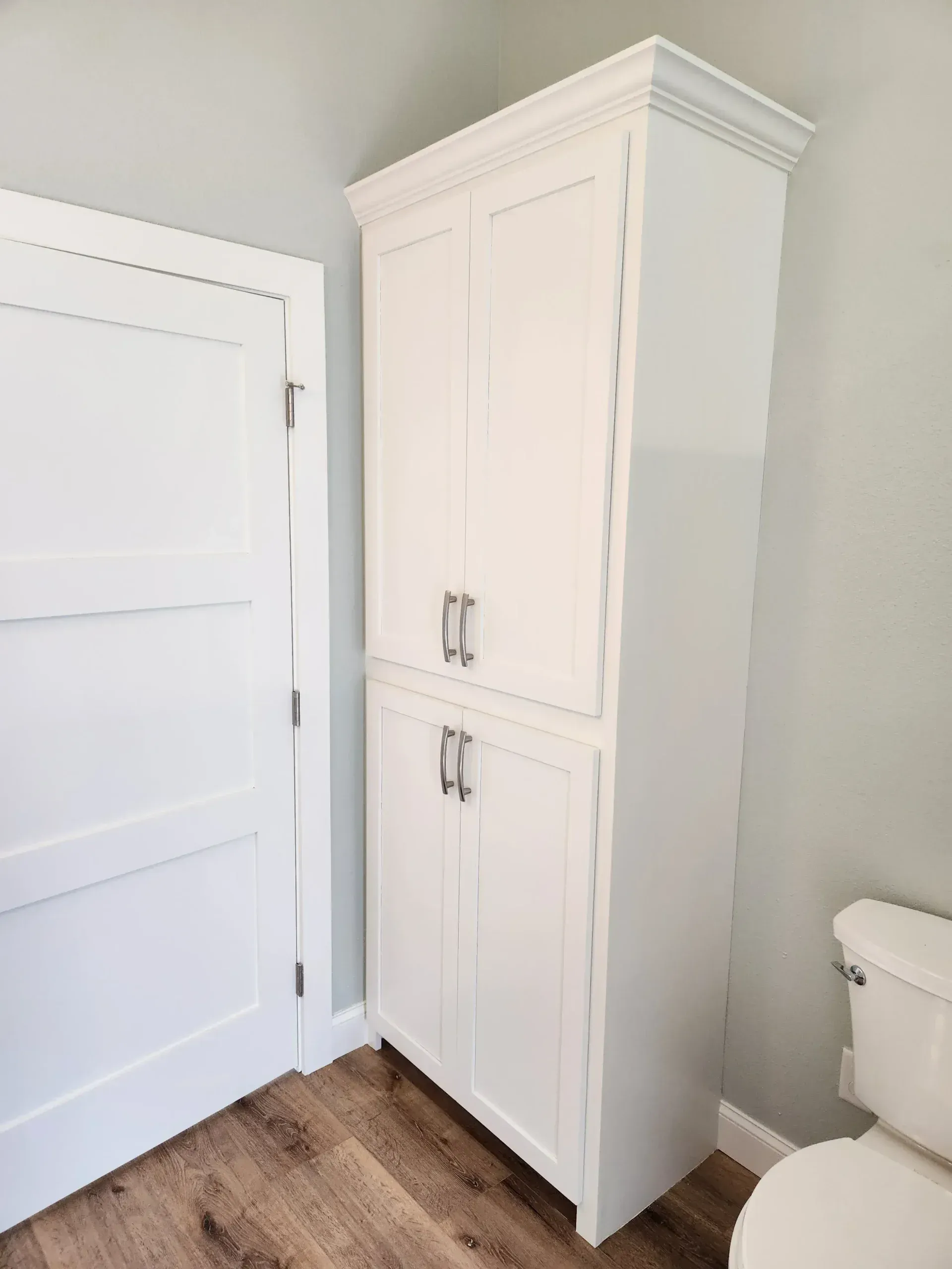 Tall white cabinet with two sets of doors, beside a white door and toilet.