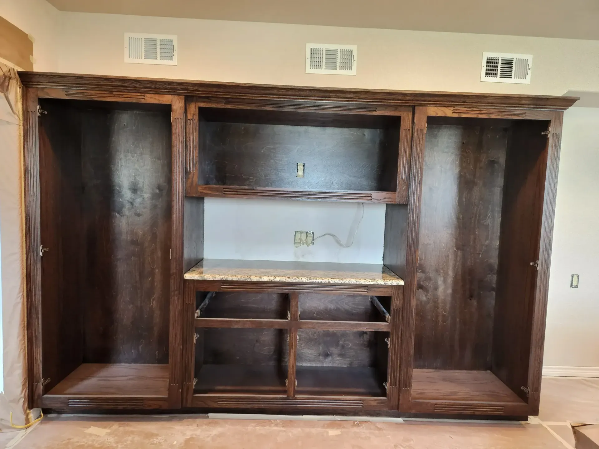Brown wooden built-in cabinet with open shelves and a granite countertop, mounted on a wall.