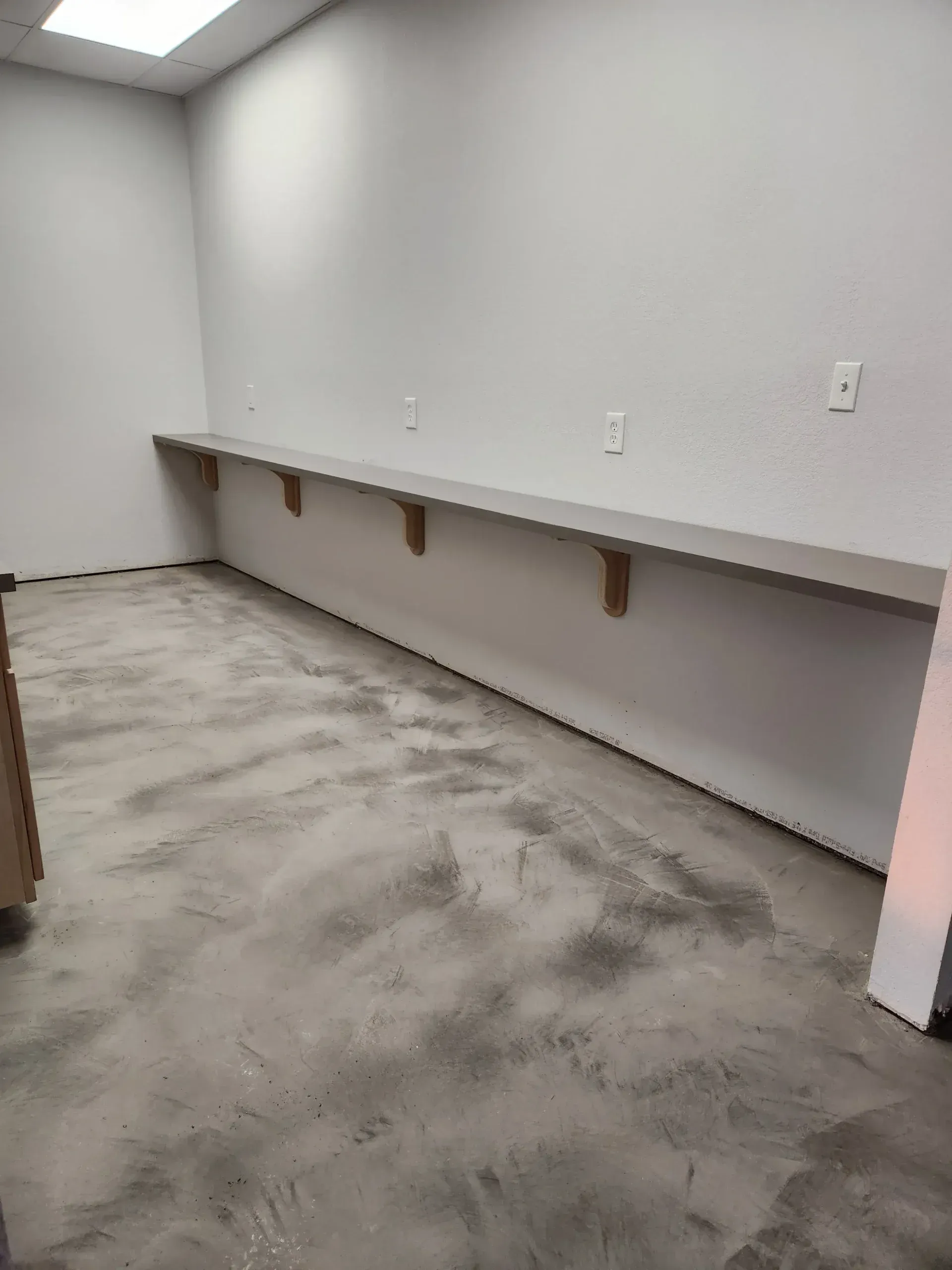 Empty room with concrete floor, gray walls, and long shelf supported by wooden brackets.