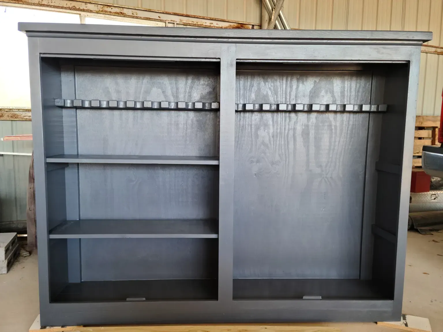 Gray wooden gun cabinet with rifle supports and shelves.