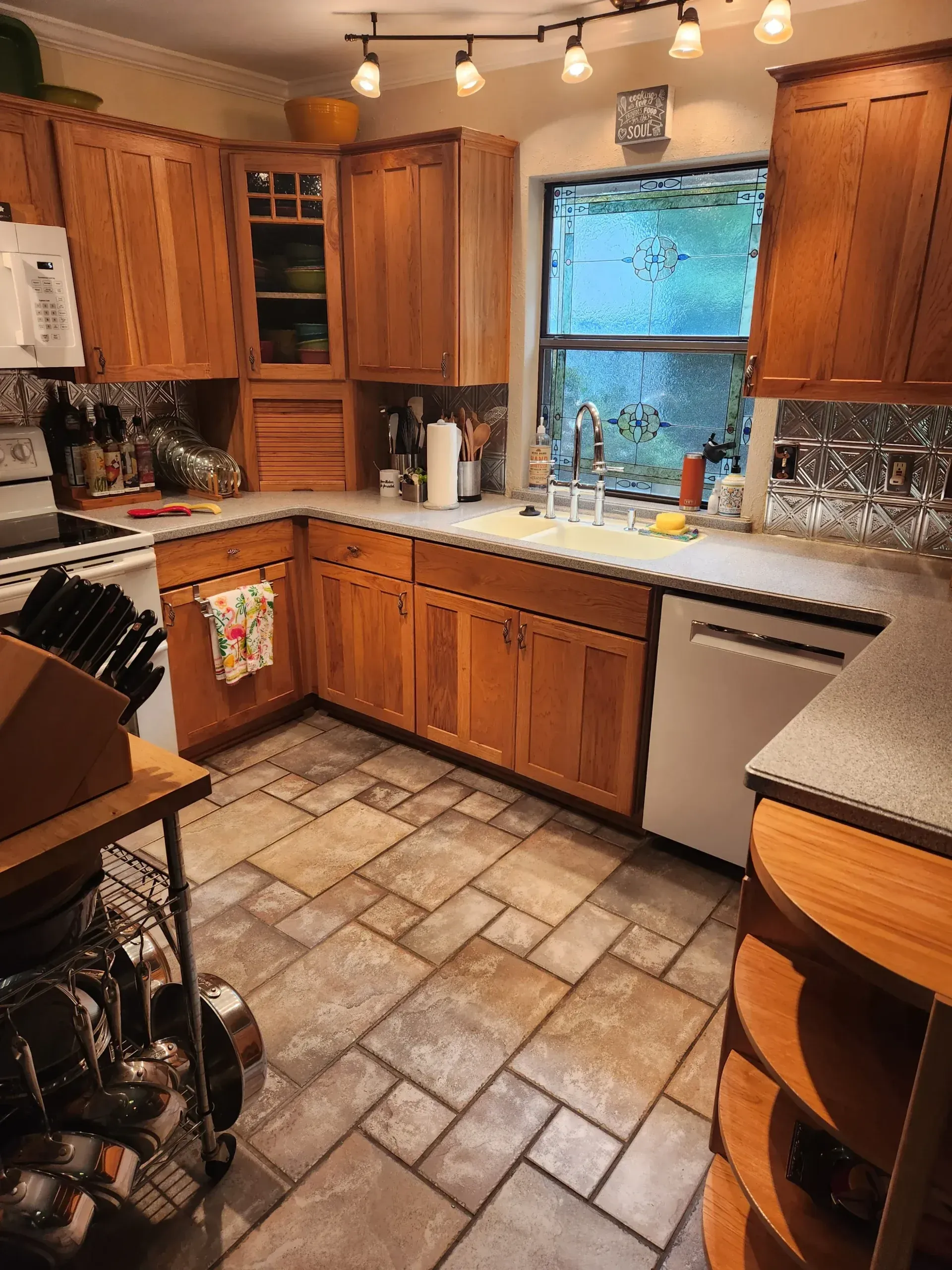 A kitchen with light wood cabinets, tiled floor, white appliances, and a window.