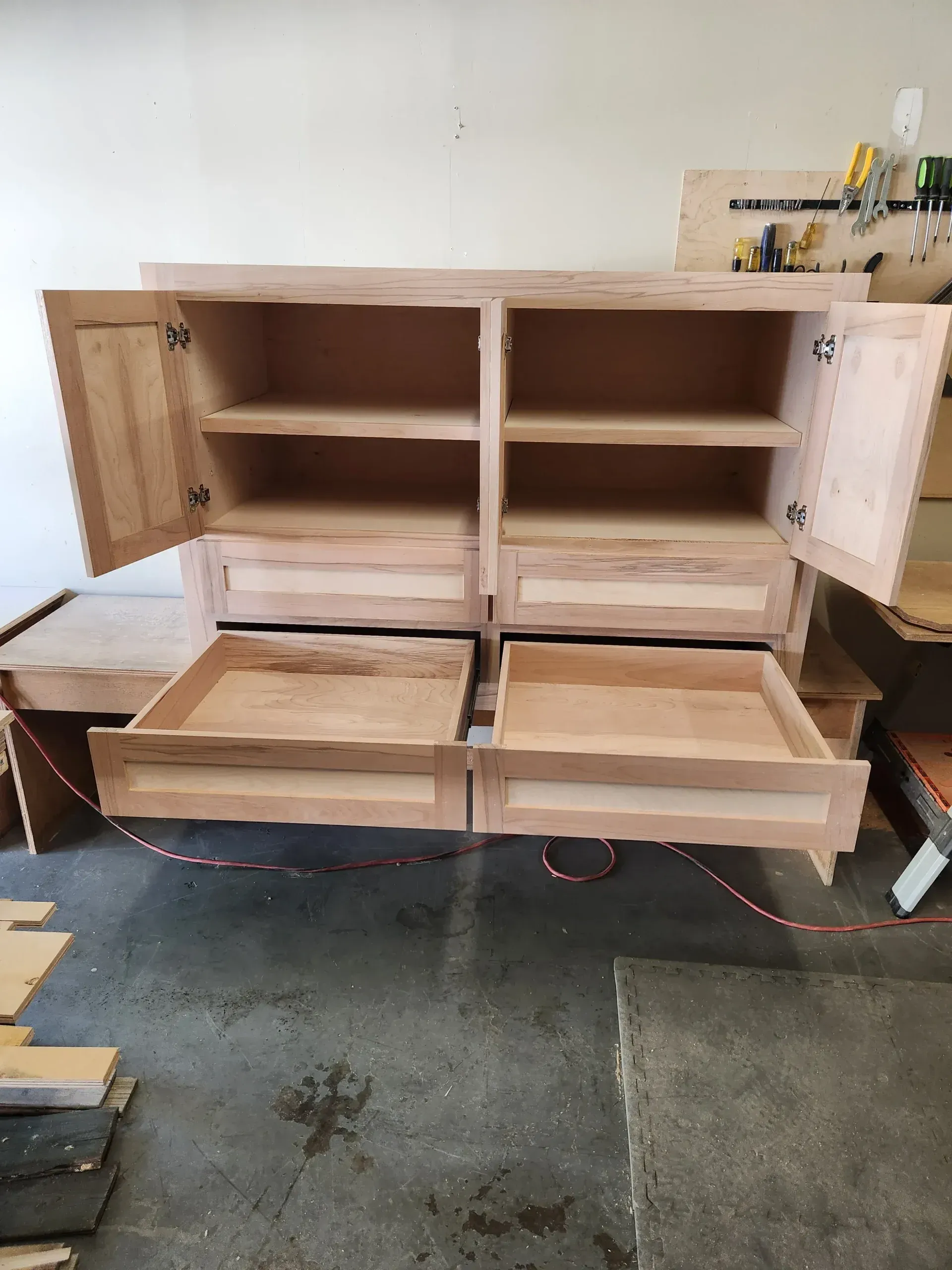 Wooden cabinet with open doors and drawers in a workshop.