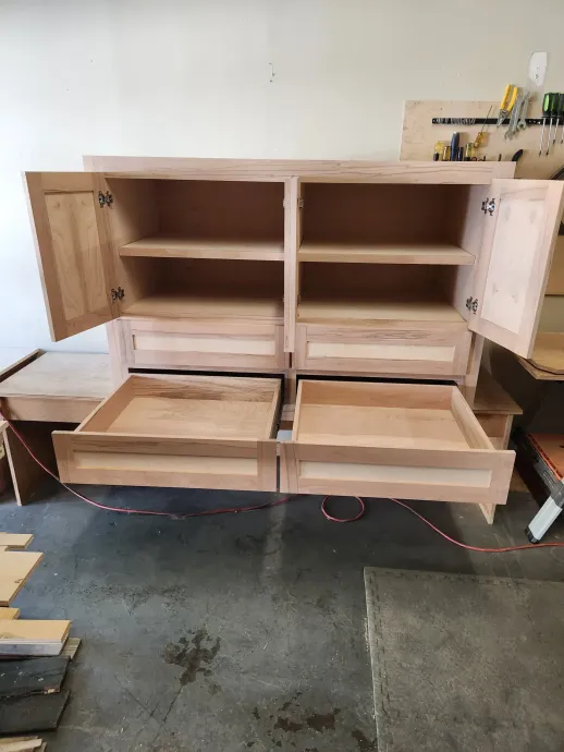 Wooden cabinet with open doors, drawers, and shelves in a workshop setting.