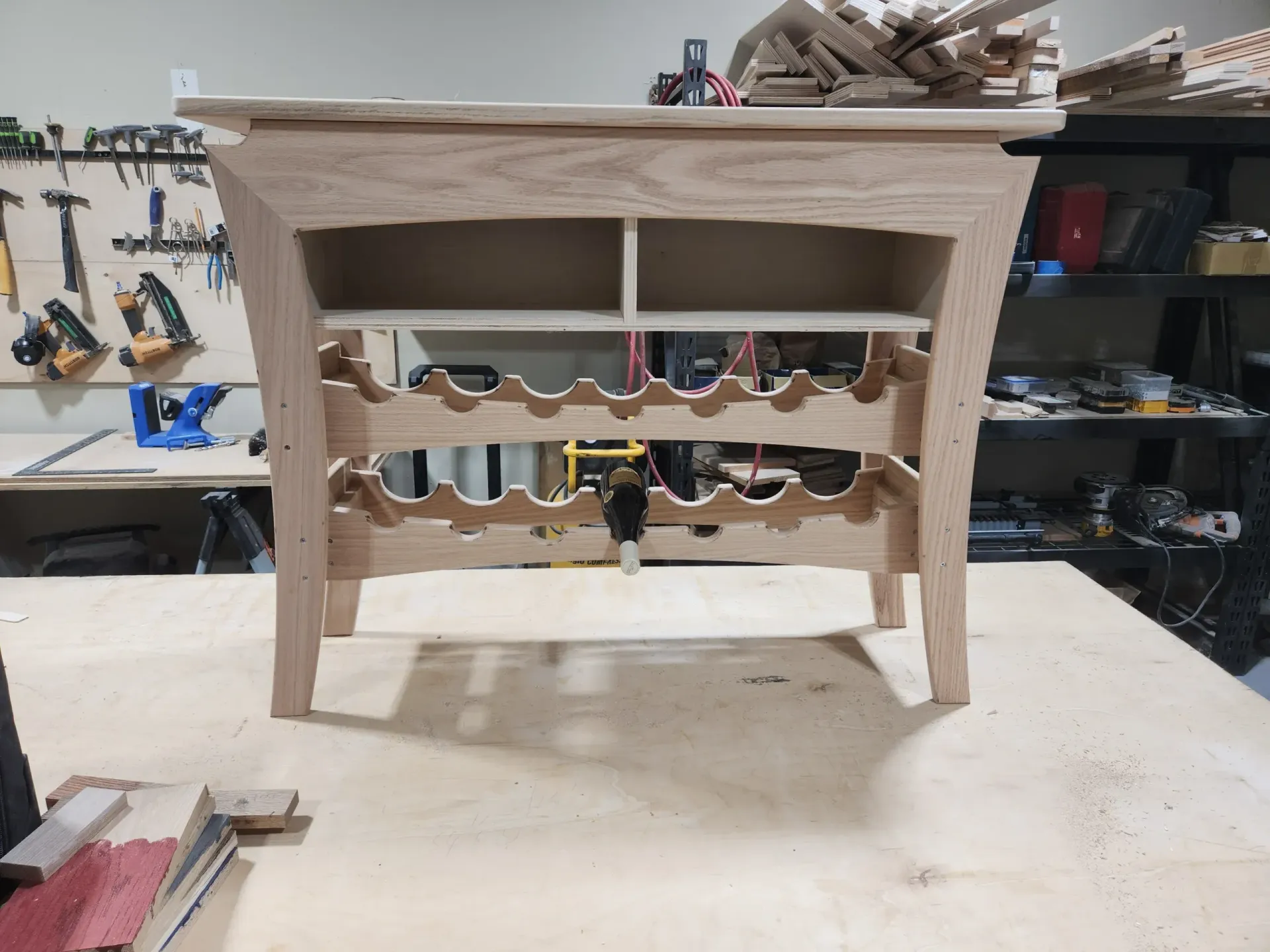 Wooden wine rack with two shelves and an upper cabinet in a workshop.