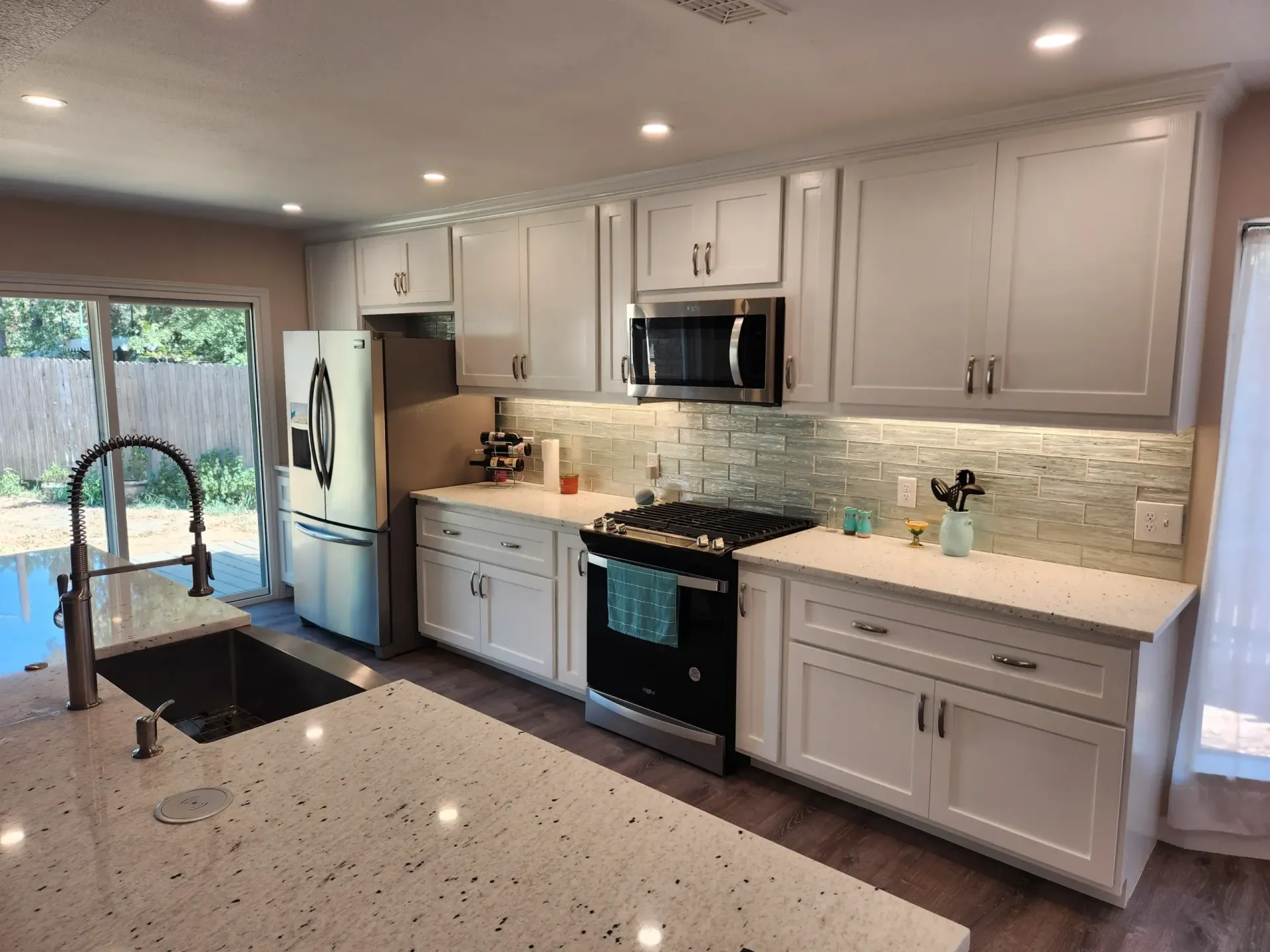 Bright, white kitchen with island, cabinets, and stainless steel appliances. Backsplash and countertops. Window and sink.