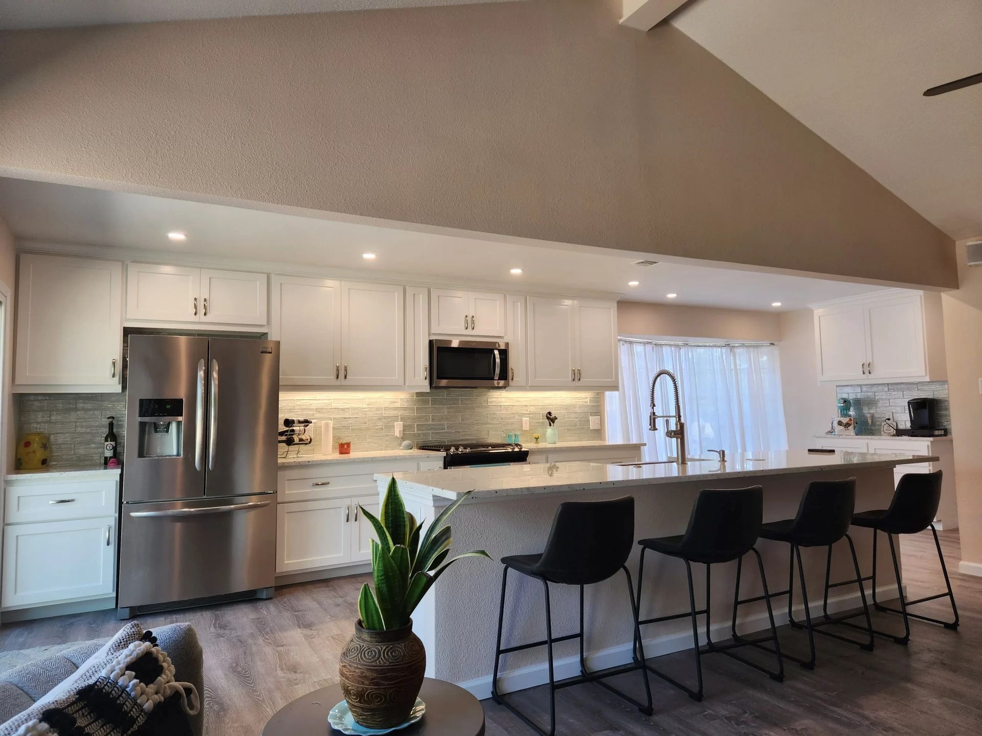 Modern white kitchen with stainless steel appliances, breakfast bar, and gray flooring.