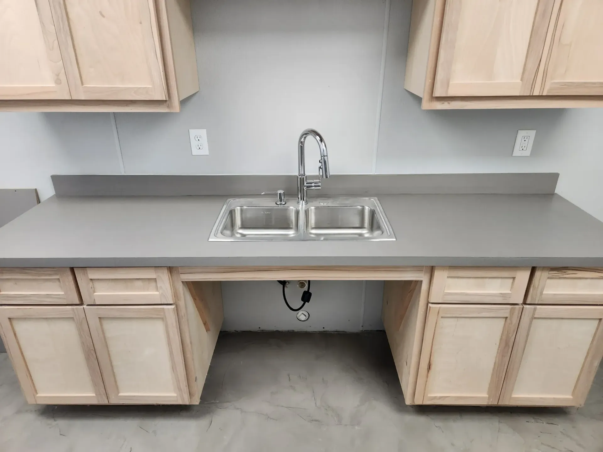 Kitchen sink with gray countertop and light wood cabinets, under-cabinet knee space.
