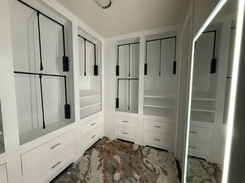 White closet with black rods, drawers, and a large mirror with a lighted frame.