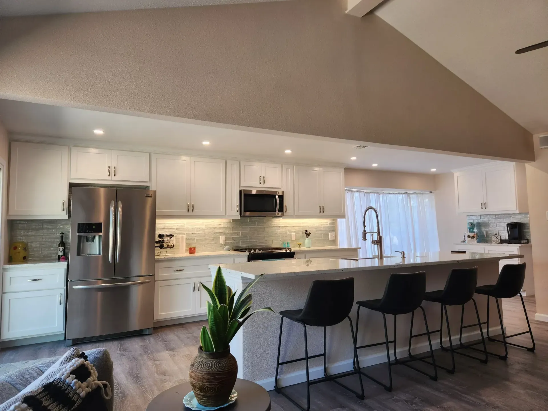 Modern kitchen with white cabinets, stainless steel appliances, and a breakfast bar with black stools.