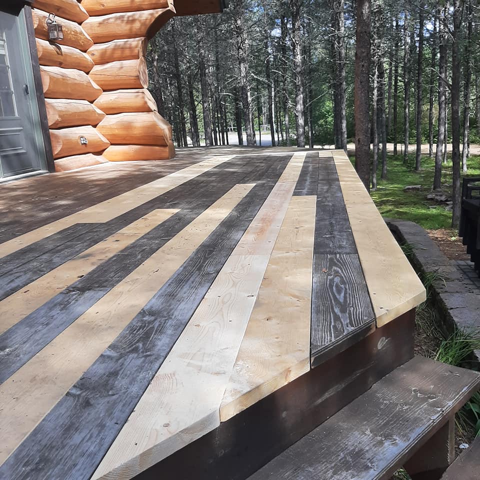 Une terrasse en bois avec une cabane en rondins en arrière-plan