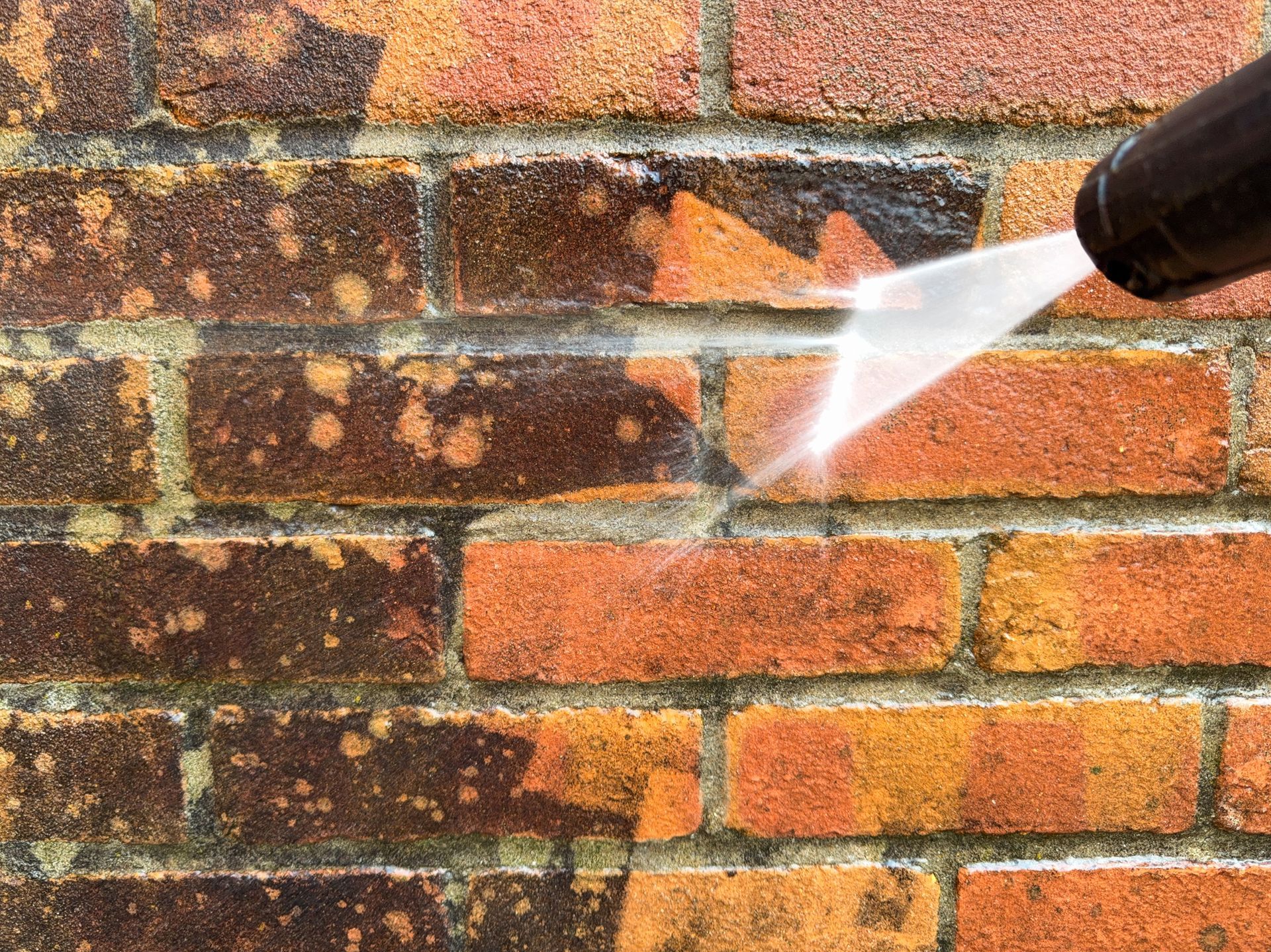 Pressure washer spraying a brick wall, cleaning off grime