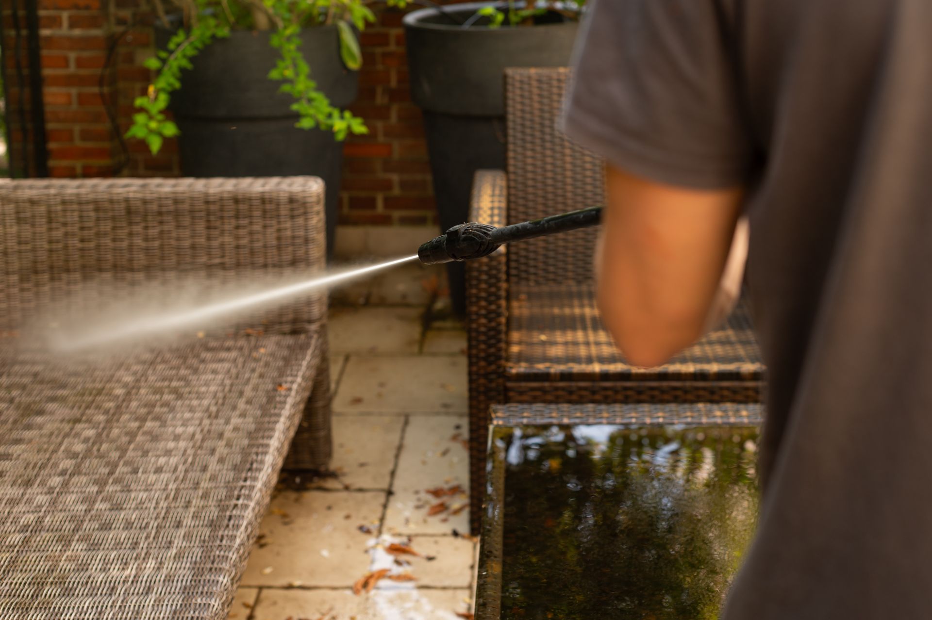 Person pressure-washing a wicker patio chair and tiled floor on a patio