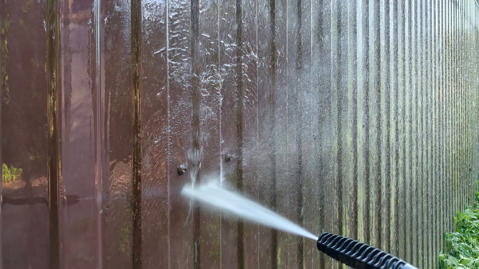 Pressure-washing a weathered wooden fence, removing dirt and grime.