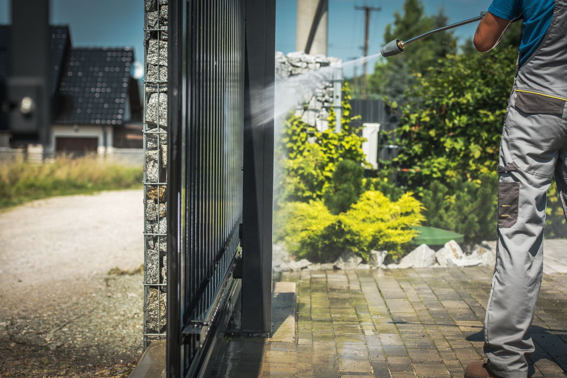 Person watering plants near a garden gate and paved walkway