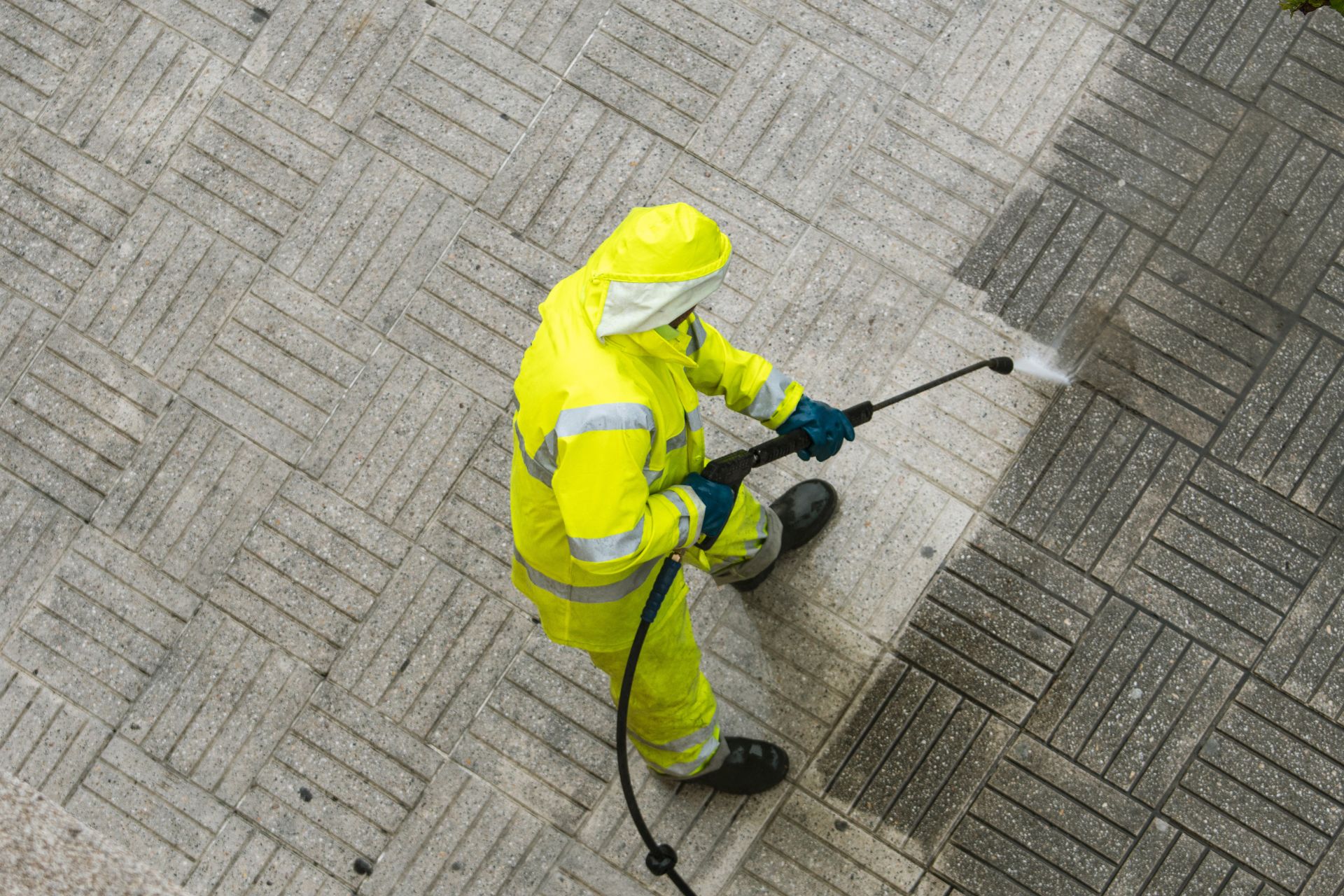 Worker in bright yellow rain gear spraying pavement with a pressure washer.