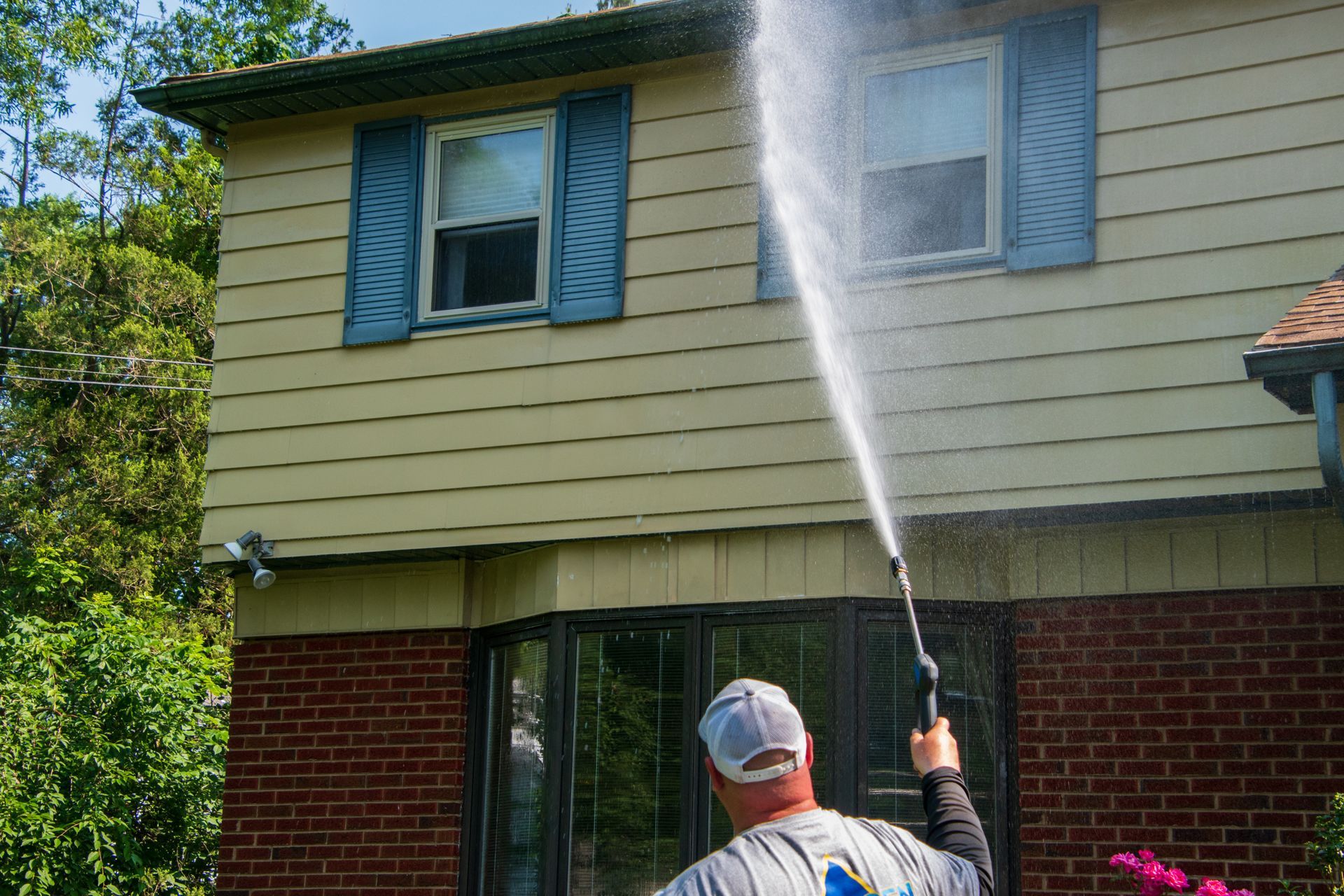 Person pressure-washing the side of a house with a spray wand and hose.
