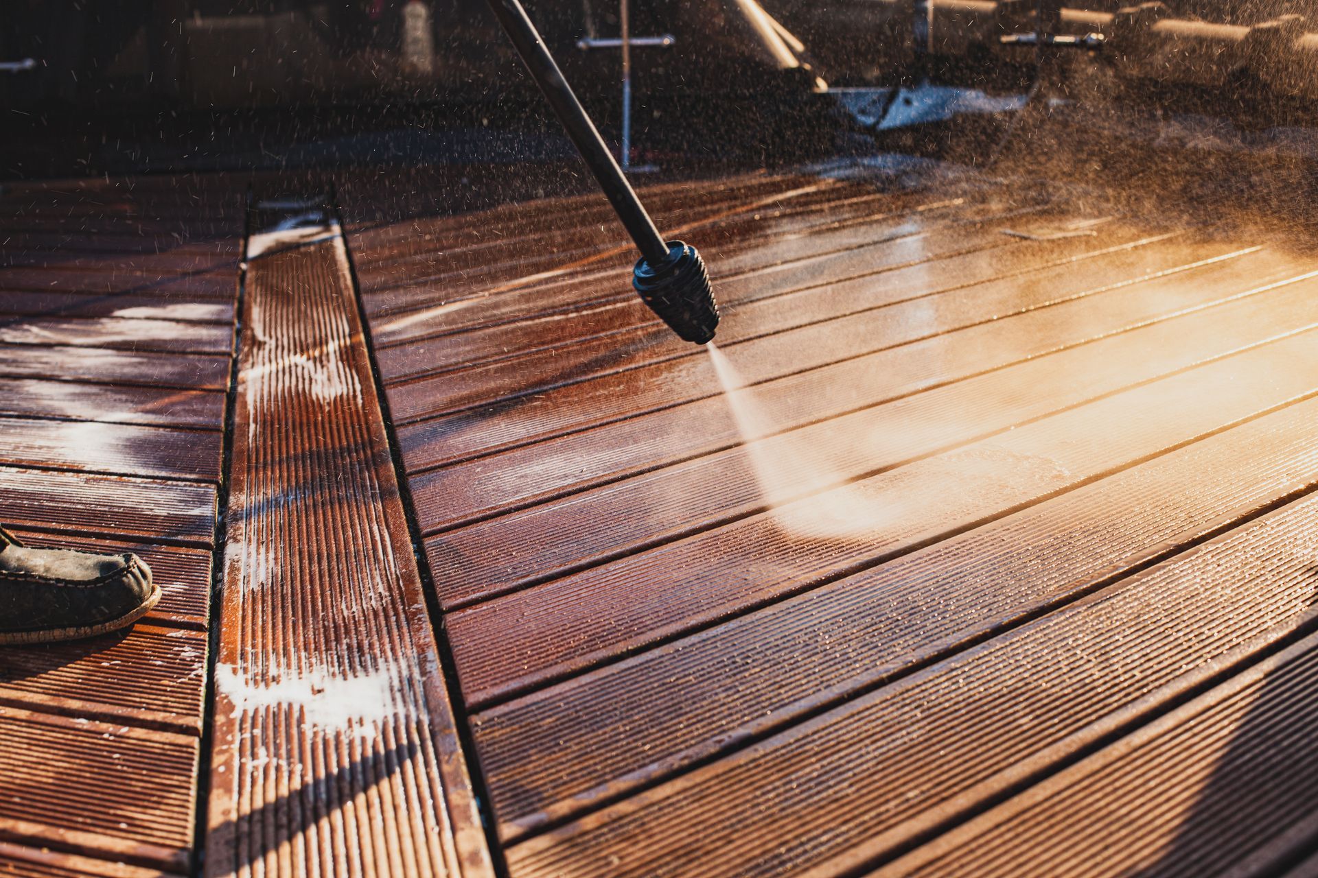 Pressure washing a wooden deck, spraying water across sunlit boards