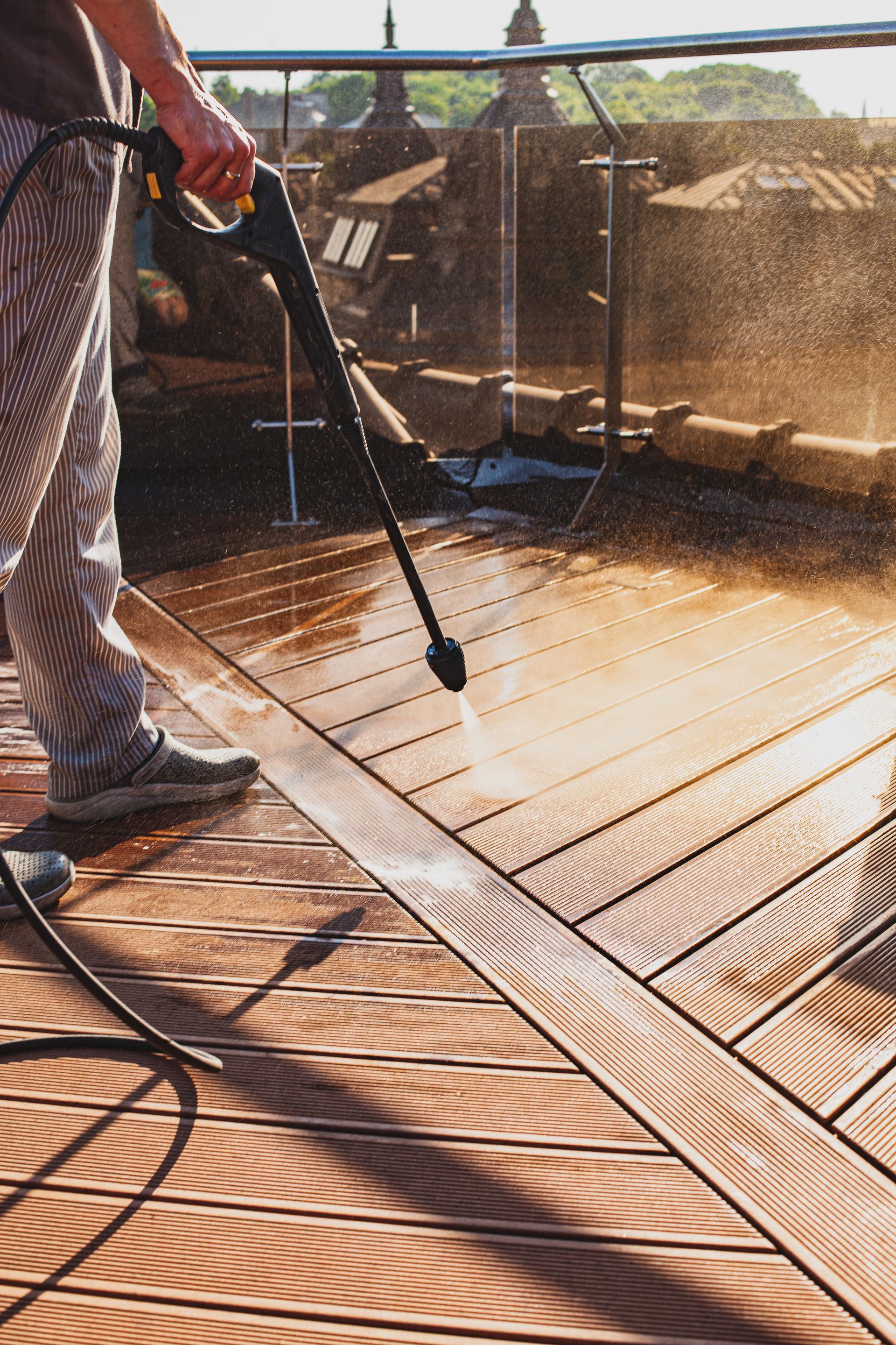 Person pressure-washing a wooden deck outdoors with a spray wand