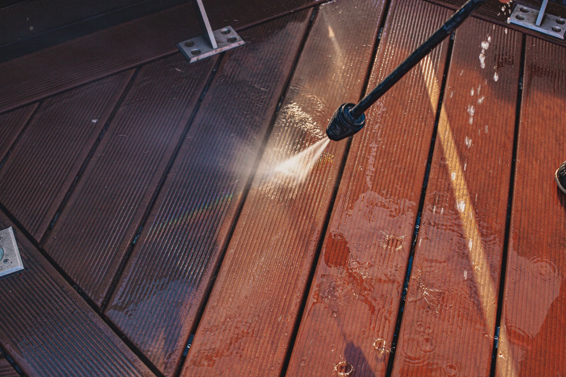 Pressure washer cleaning a wet wooden deck with diagonal planks and bright sunlight.