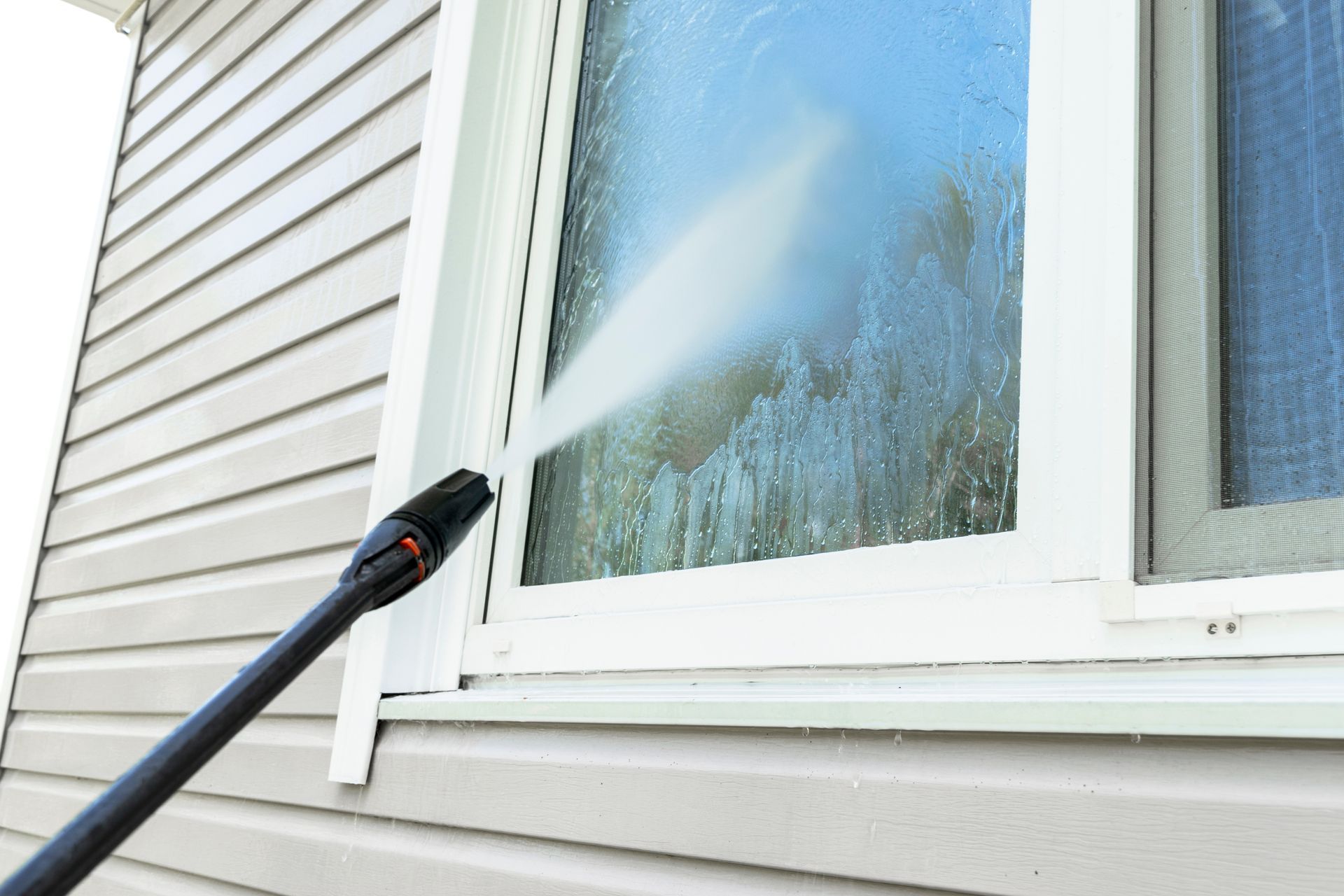 Pressure washer spraying a house window and siding