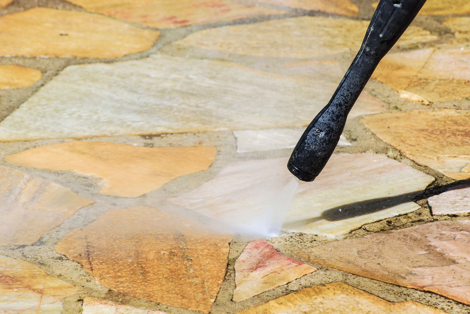 Pressure washer cleaning a stone patio with a spray nozzle close to the surface