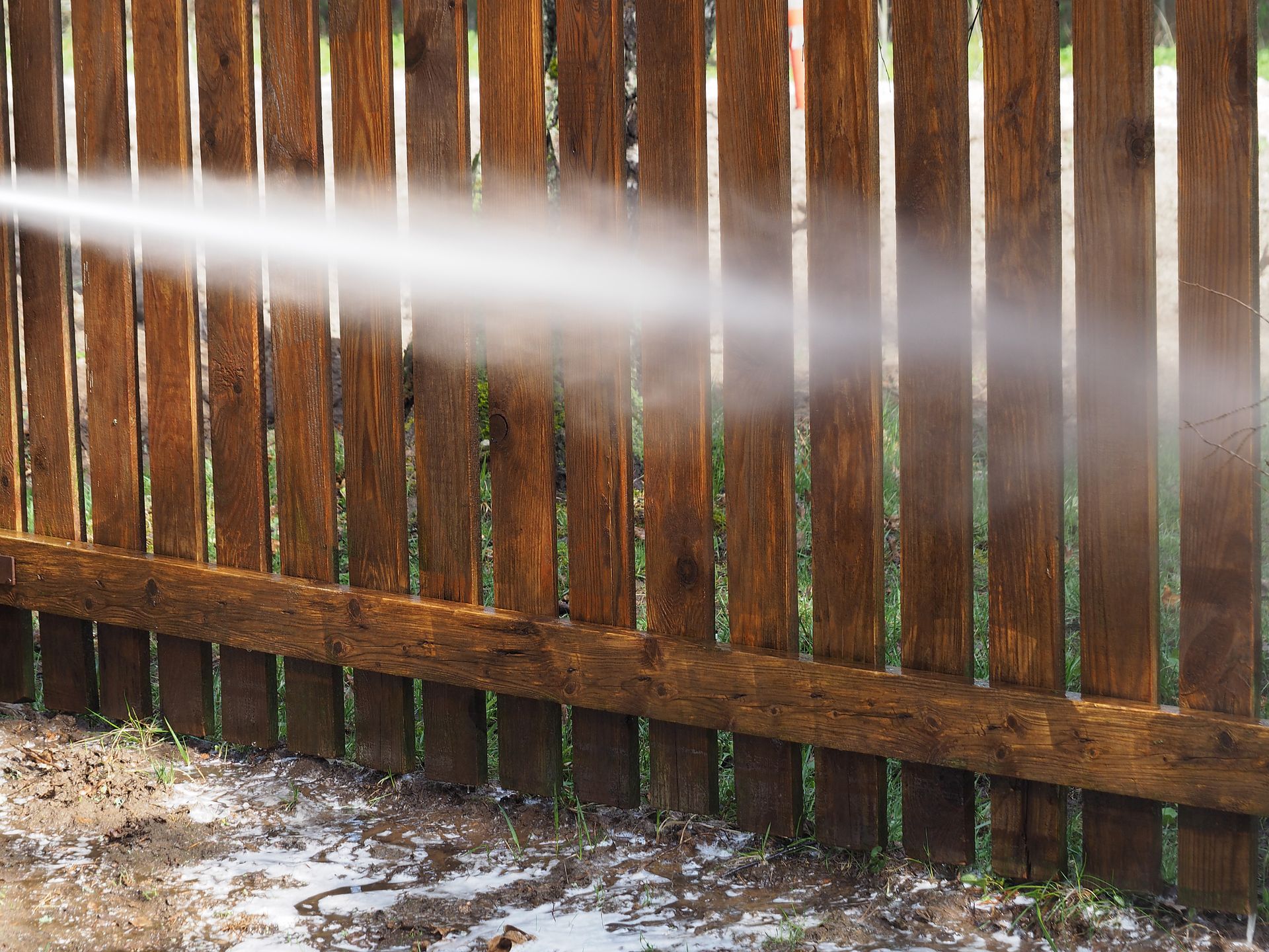 Water spraying across a wooden fence in an outdoor yard, with puddles on the ground.