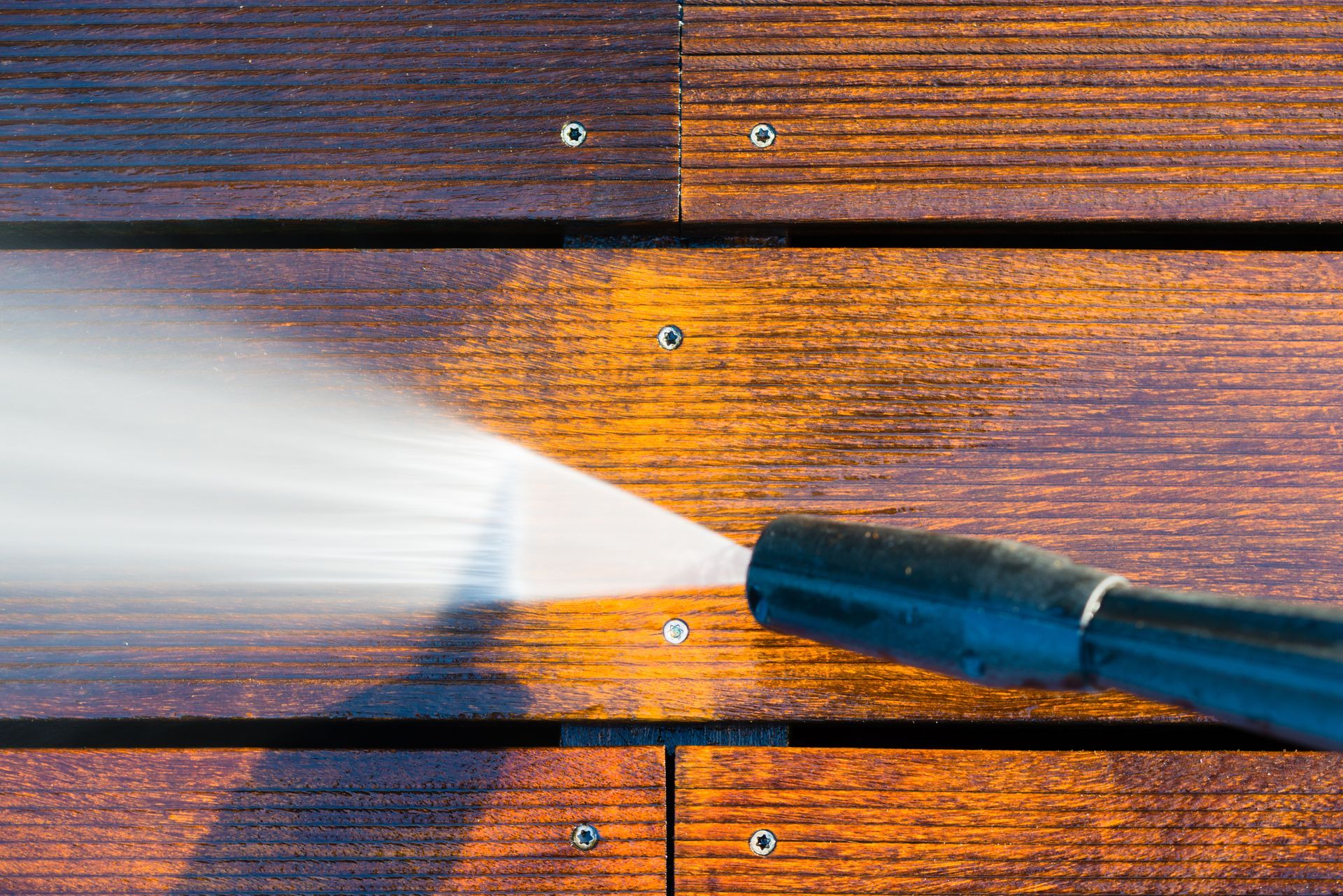 Pressure washer spraying water onto a wooden deck, creating a bright mist and wet, cleaned boards
