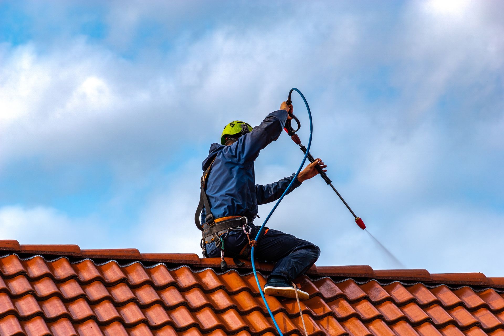 Roofer in safety gear climbing a red-tiled roof against a cloudy sky