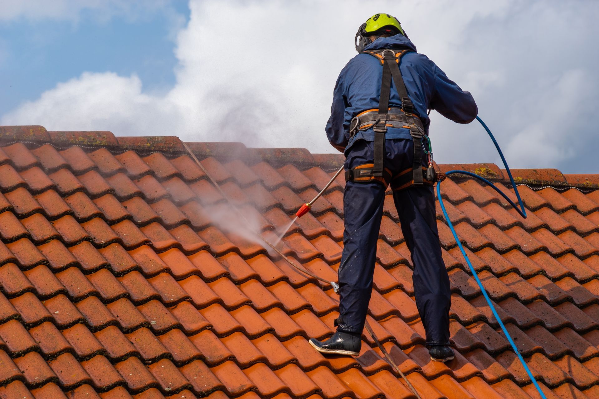 Worker power-washing a red tiled roof under a cloudy sky