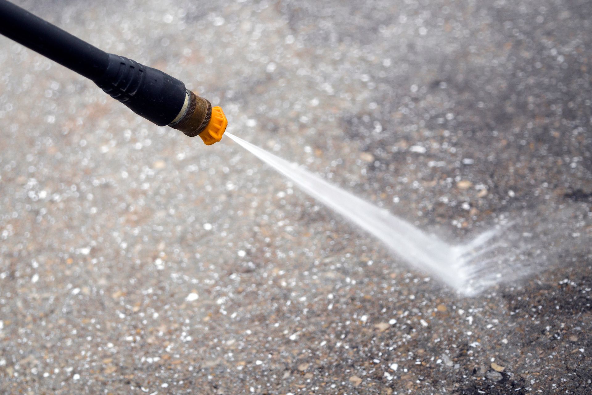 A garden hose sprays a strong stream of water across a wet pavement