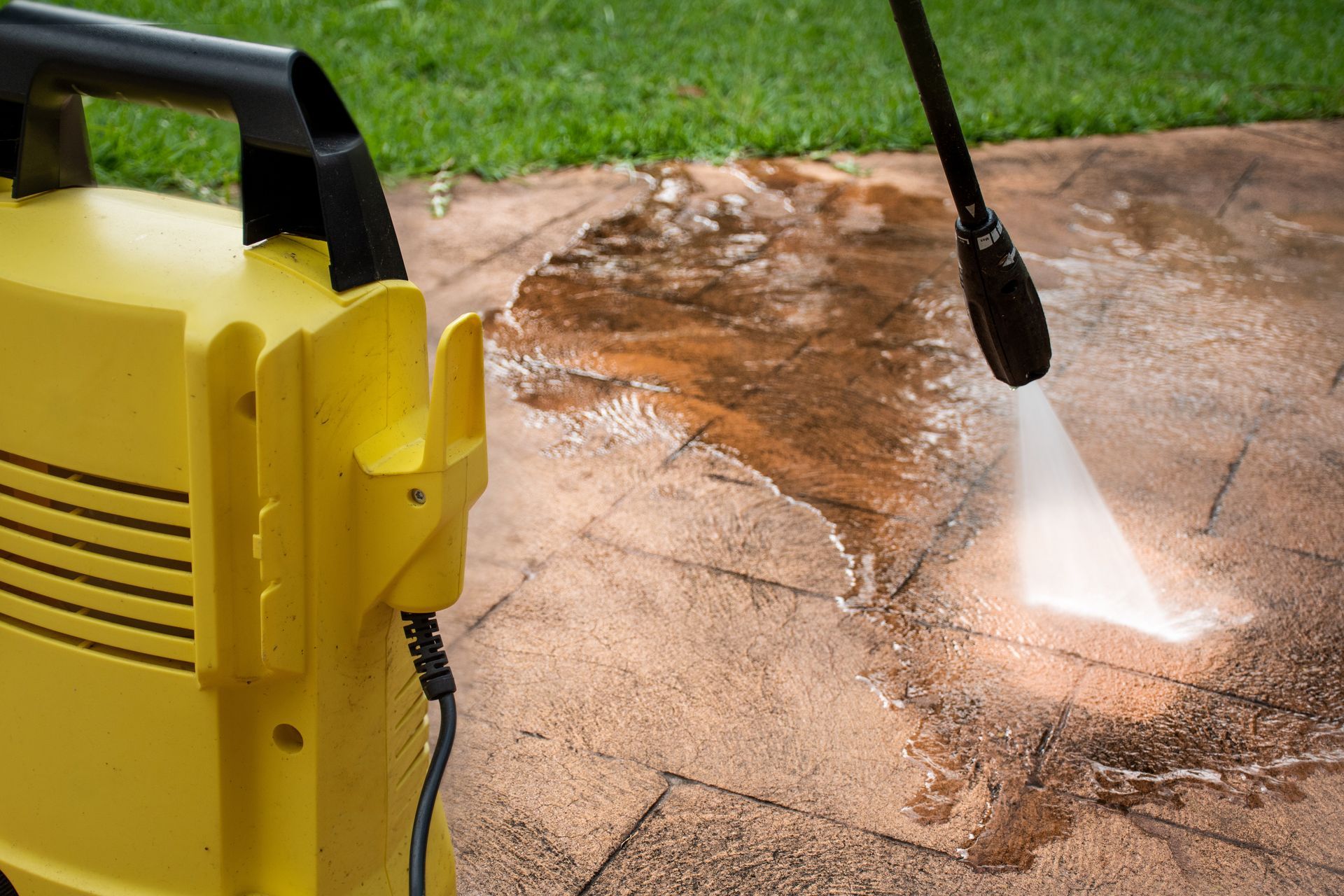 Yellow pressure washer spraying water onto a dirty concrete patio outdoors