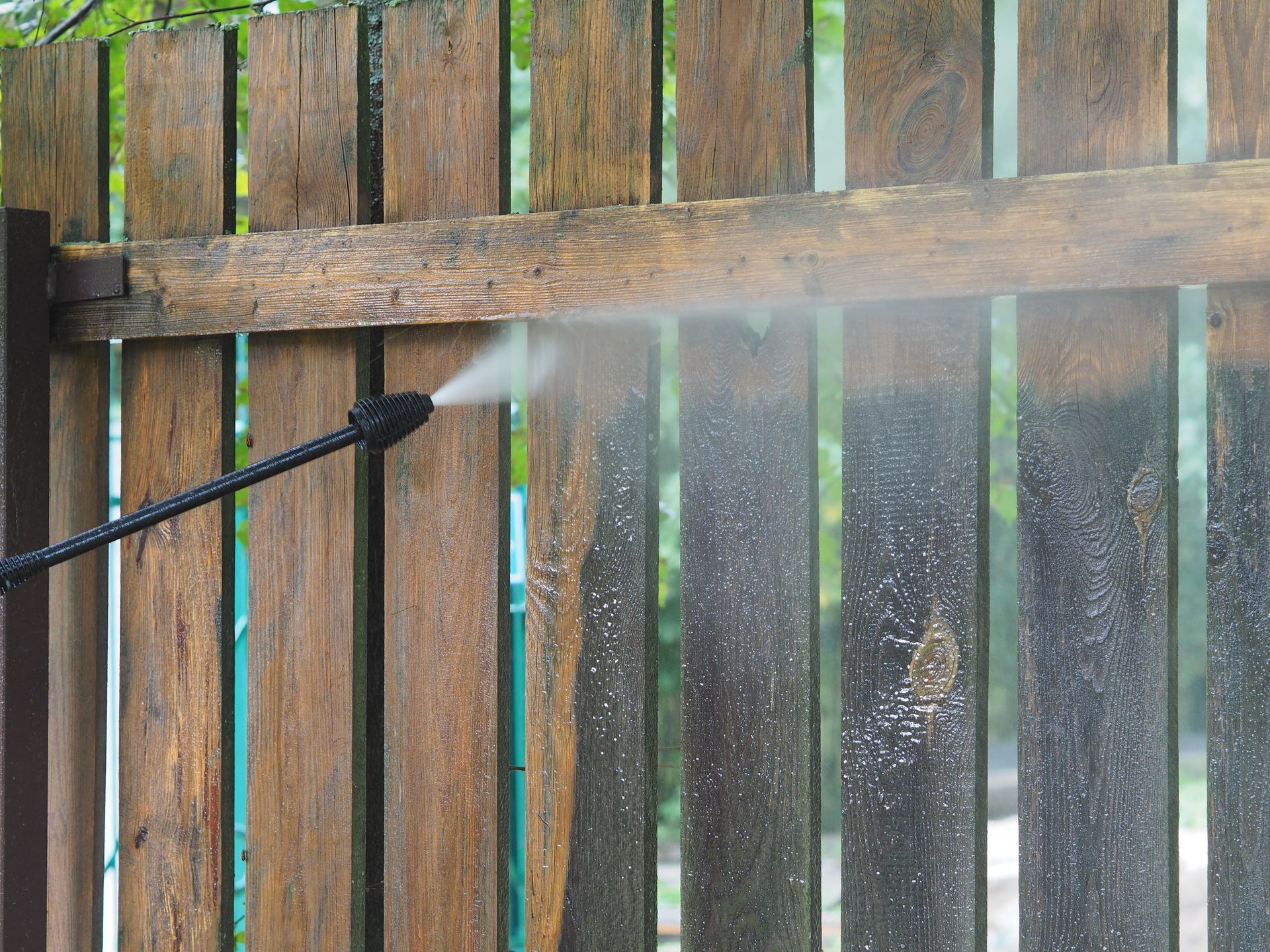 Pressure washer spraying water on a wooden fence, creating a mist.
