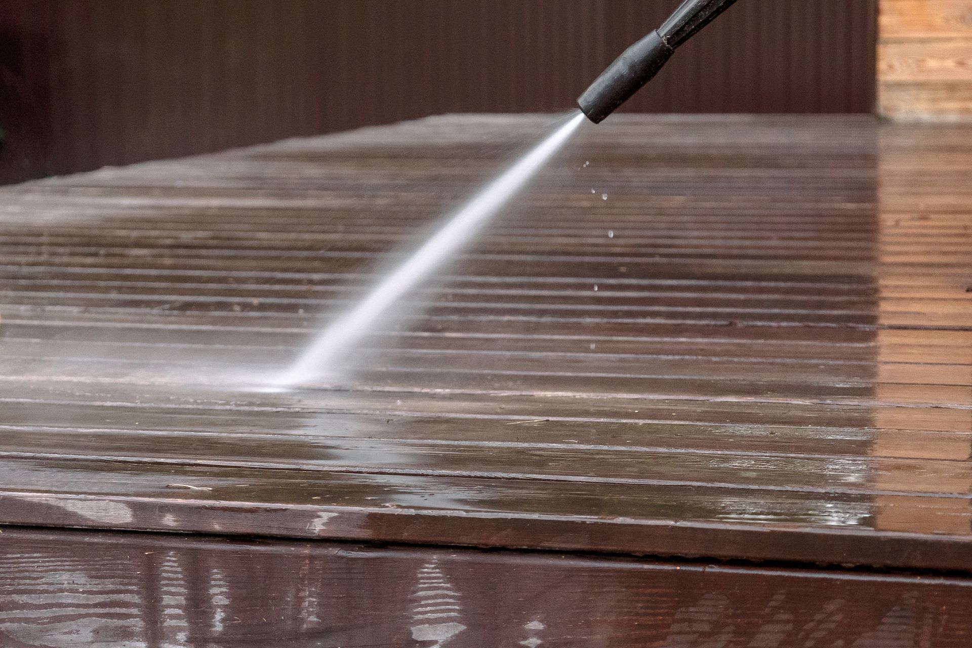 Pressure washer spraying water across a wet wooden deck surface.