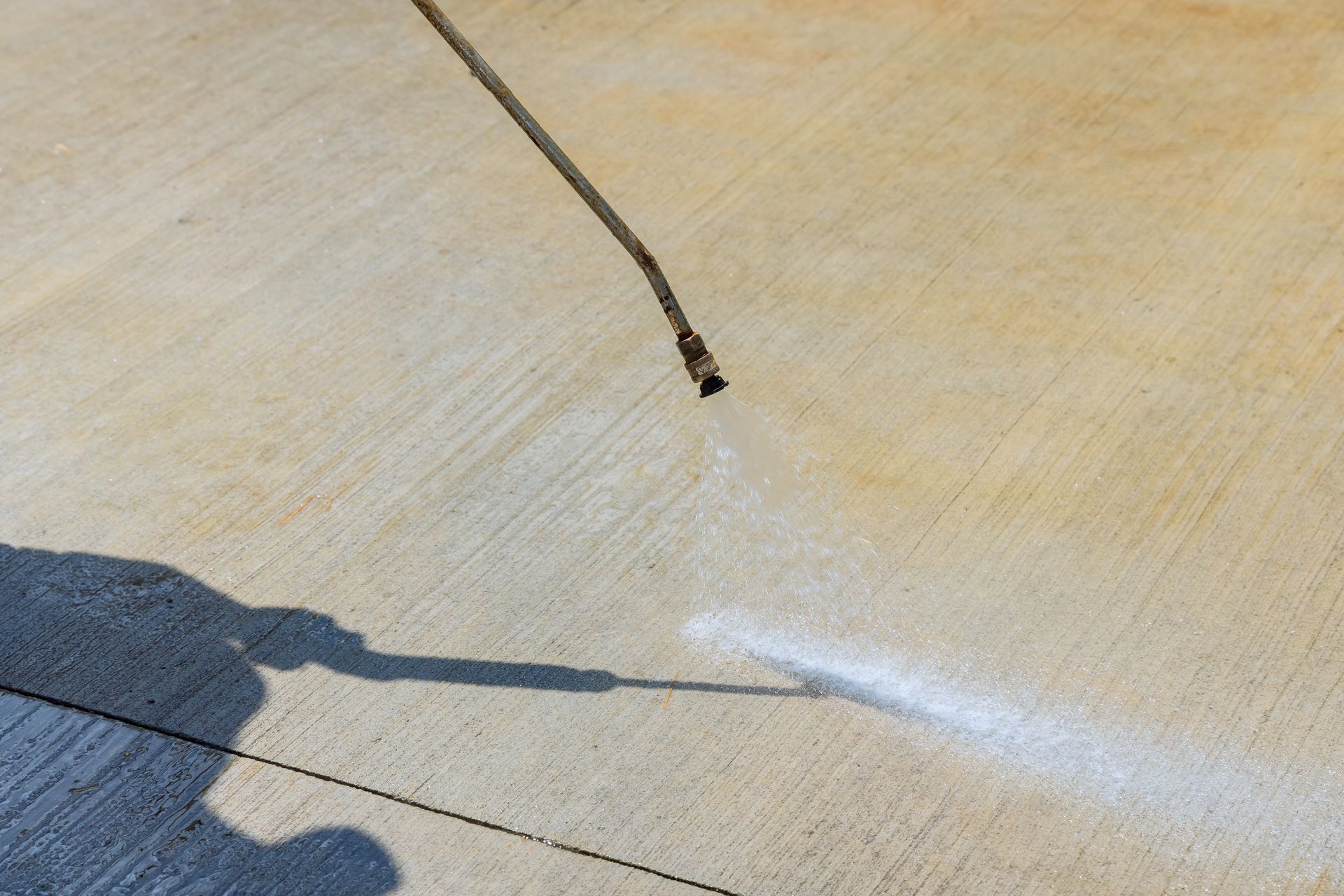 A hose sprays water across a sunlit concrete surface, creating a white mist on the ground.