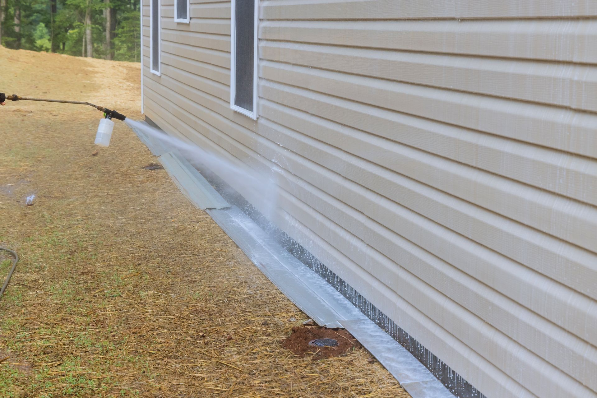 Water spraying along the foundation of a beige house beside a gravel yard