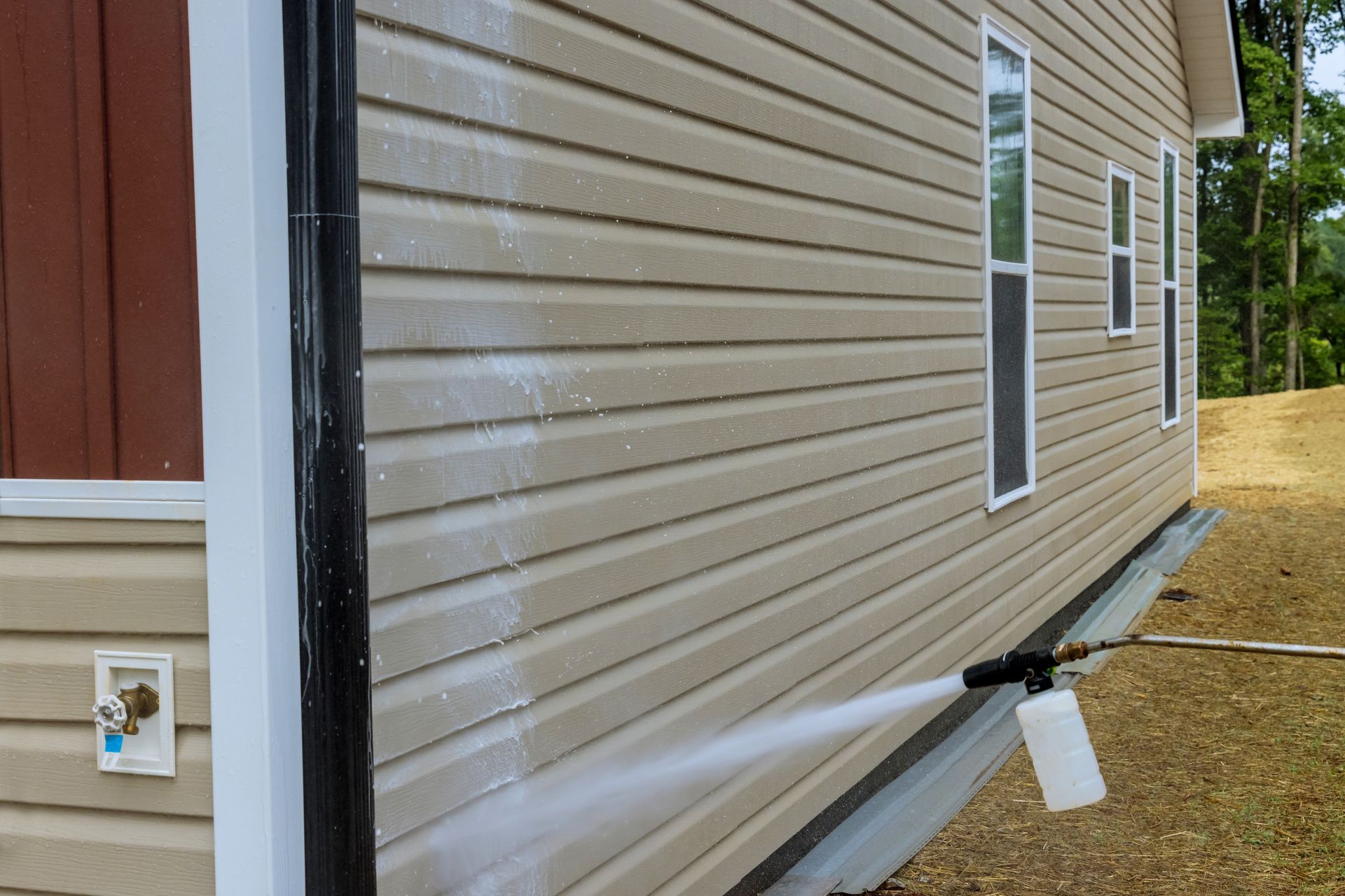 Side view of a beige house with vinyl siding, windows, and a foundation drainage pipe near a gravel yard
