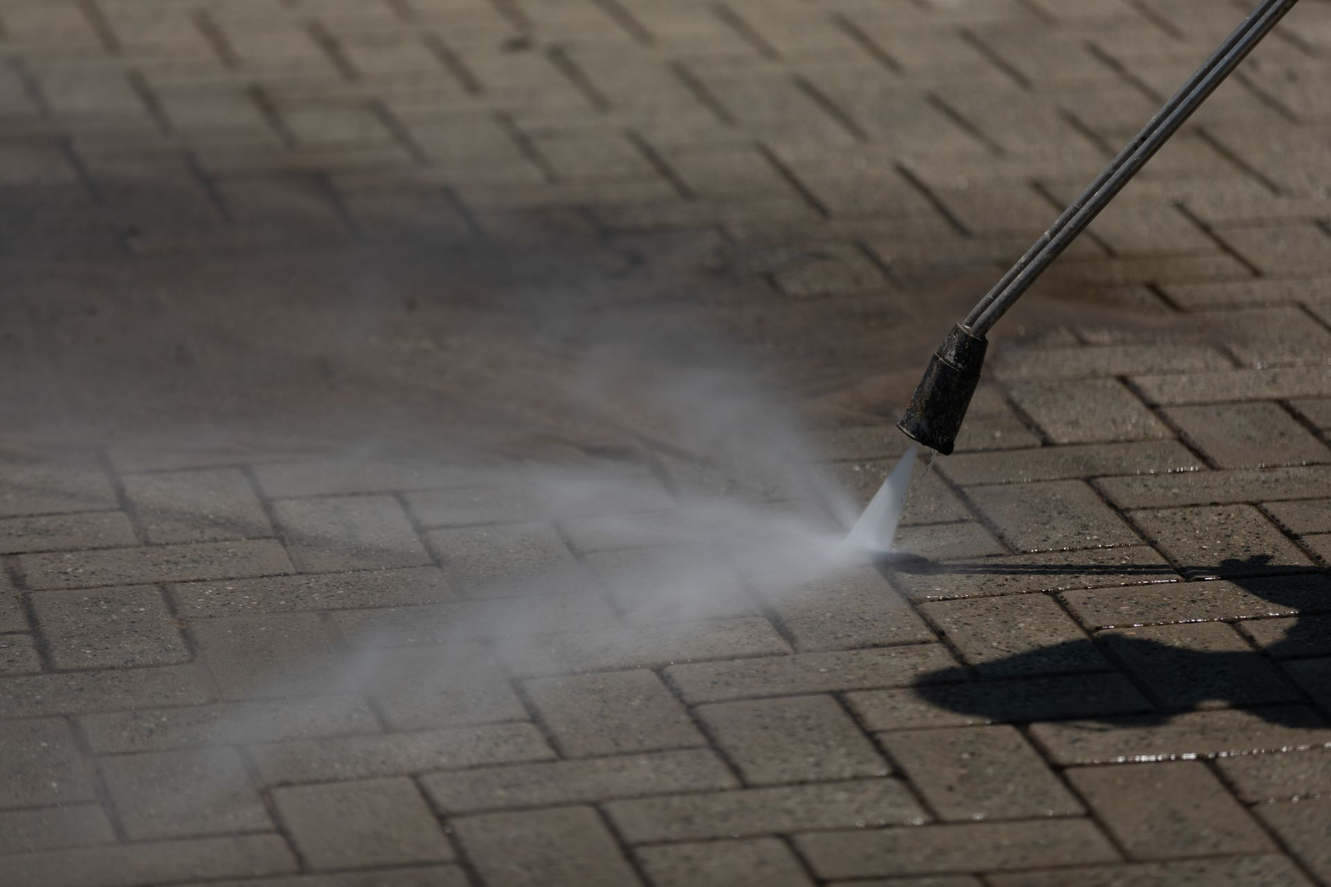 Person pressure-washing a brick pavement with a spray wand