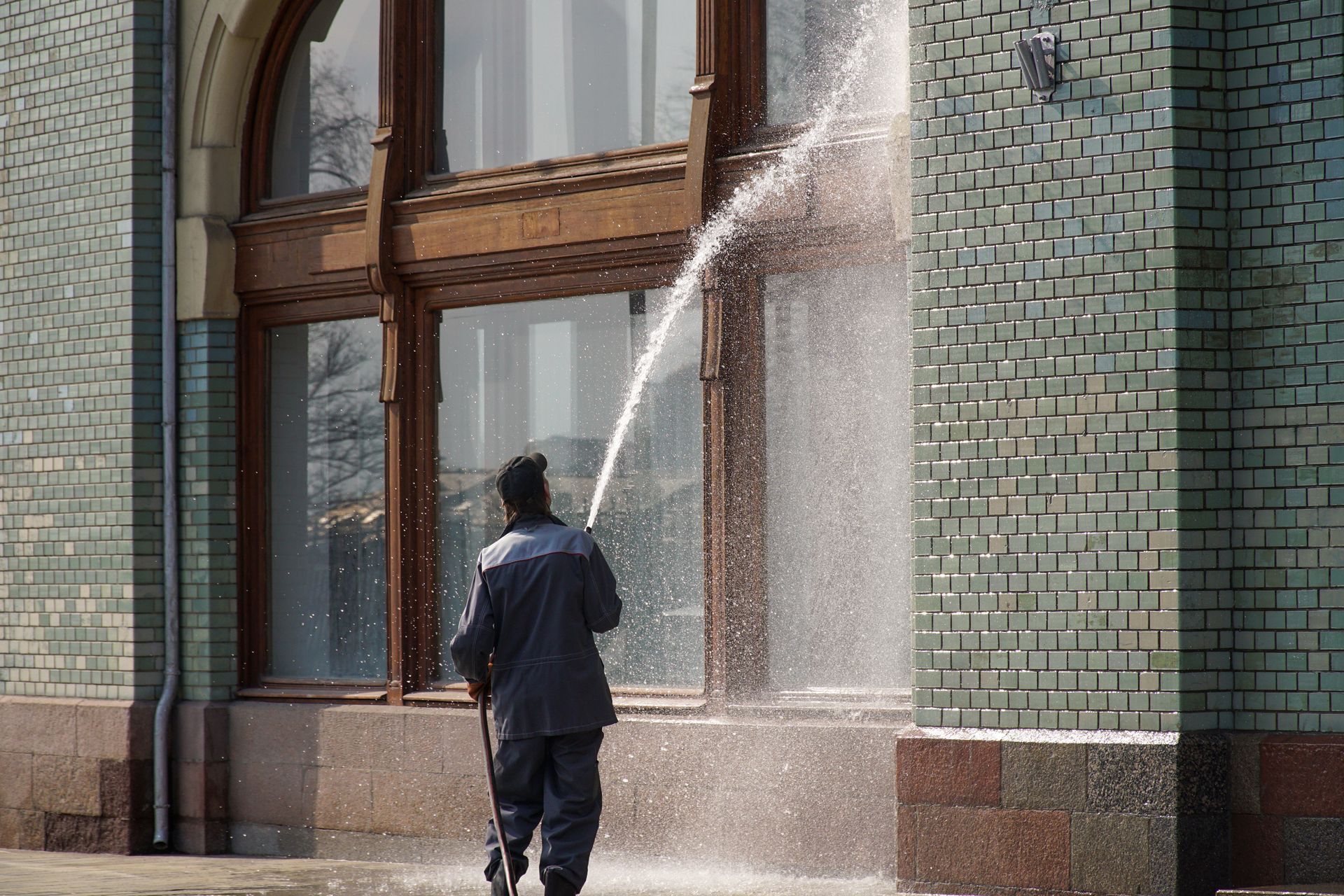 Person spraying water on a brick building exterior with large windows