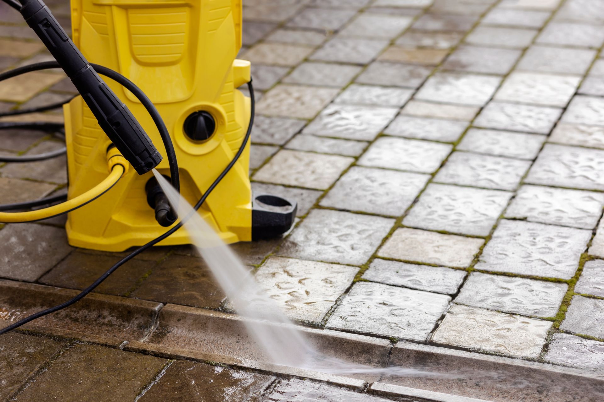 Yellow pressure washer spraying water onto a paved driveway