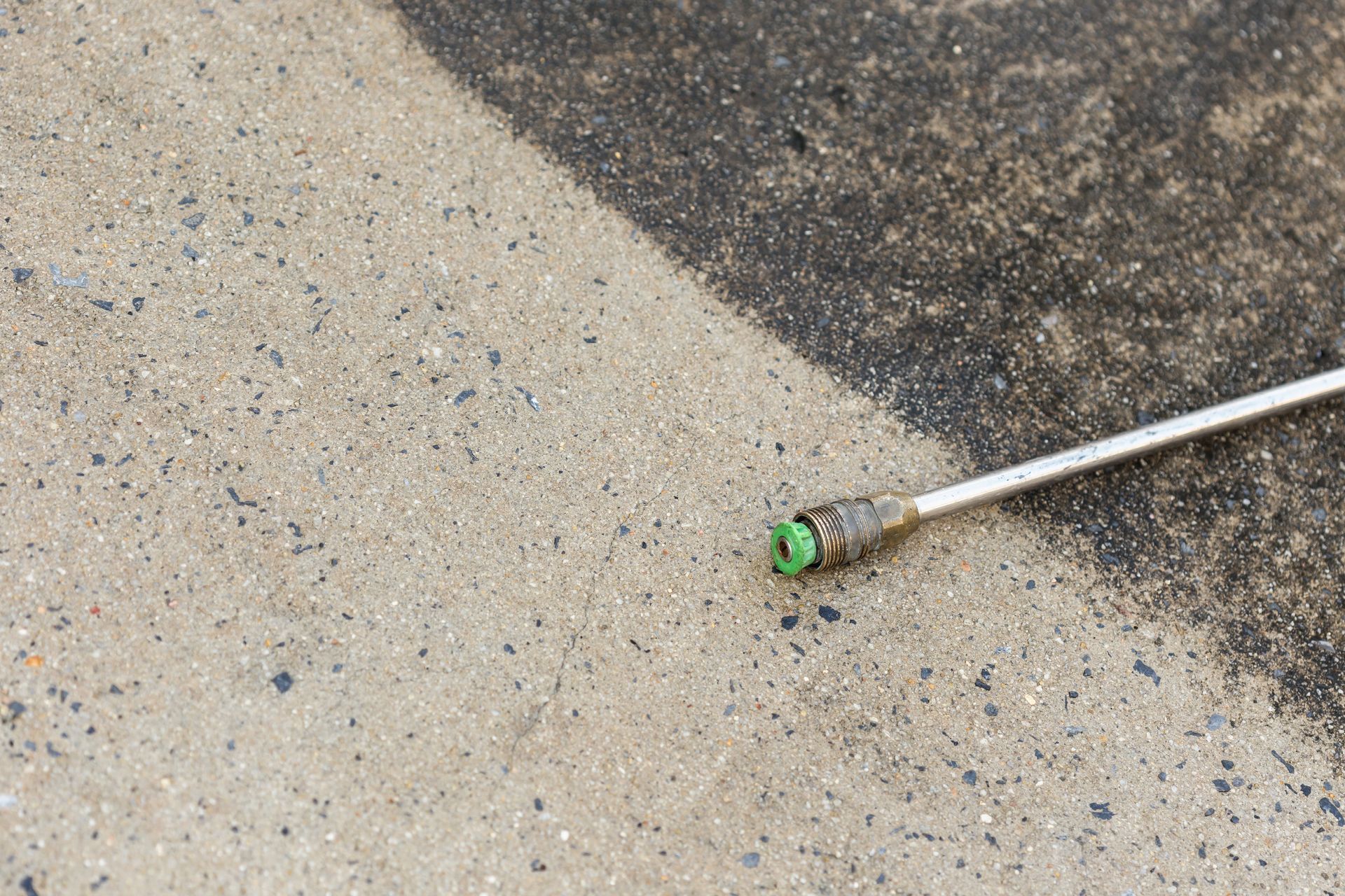 Green weed trimmer head on a concrete surface next to dark asphalt edge