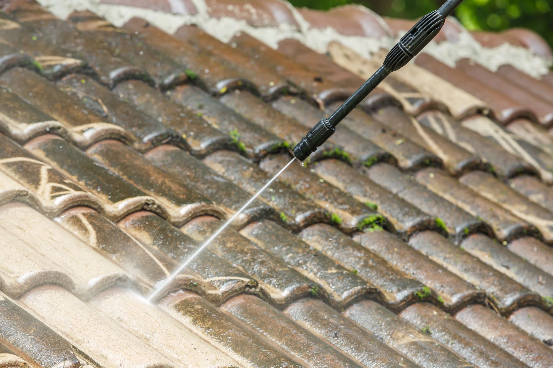 Pressure washing a tiled roof with a spray wand, removing dirt and moss
